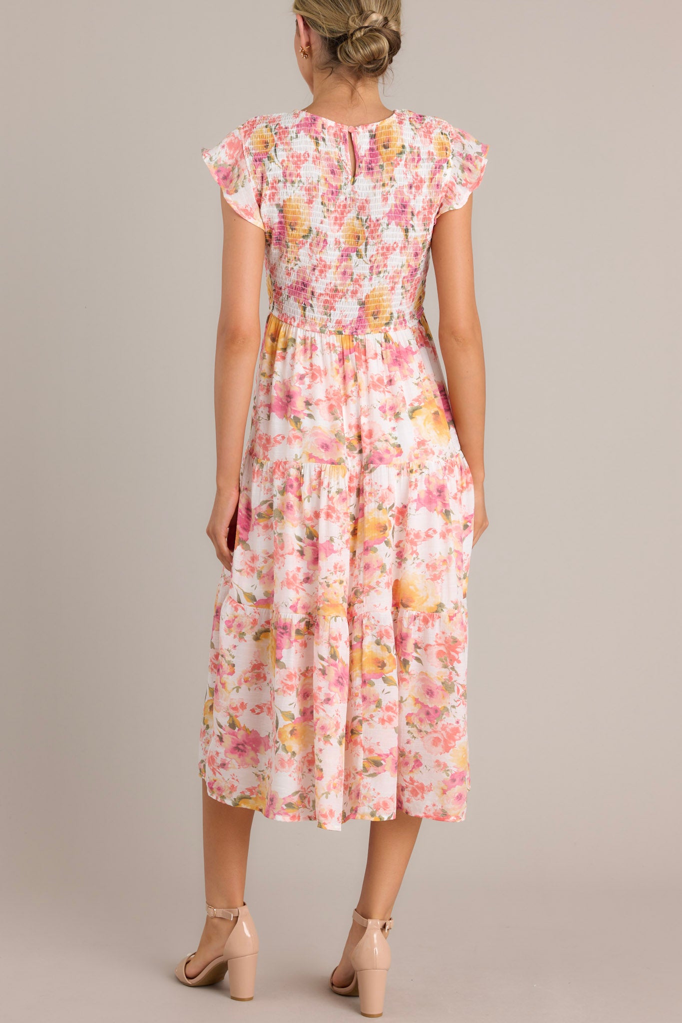 Back view of this pink floral midi dress featuring a high neckline, flutter sleeves, and a tiered design.