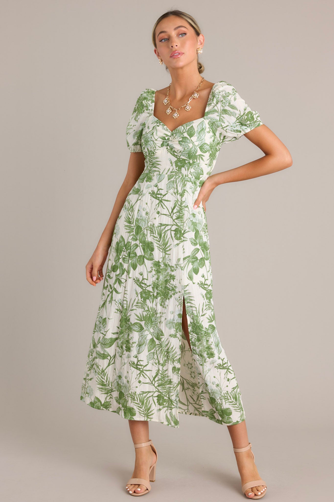 Green floral midi dress showcasing short puff sleeves, a sweetheart neckline, fitted bodice, cinched waist, and a front slit on a mid-length skirt.