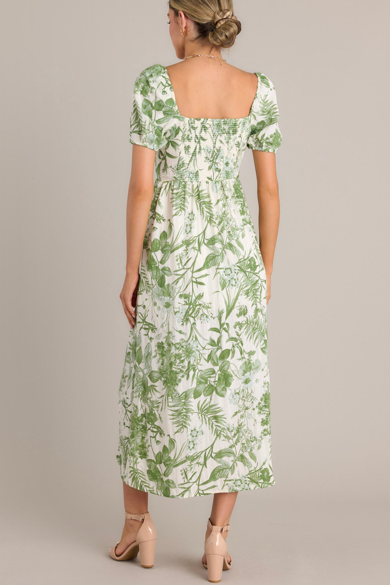 Back view of this green floral midi dress featuring short puff sleeves, a fitted bodice, cinched waist, and a mid-length skirt with a green botanical print.