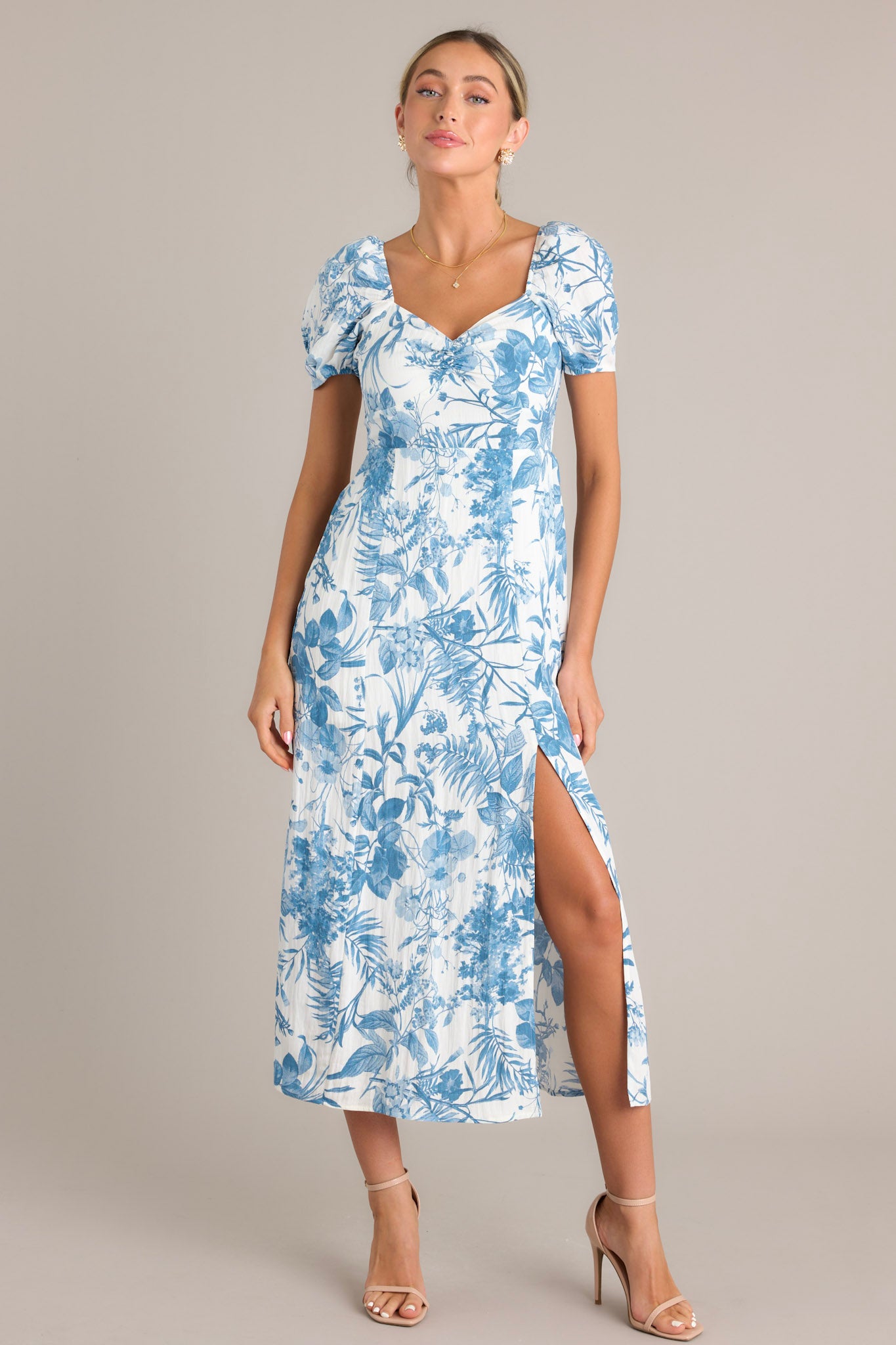 Blue floral midi dress showcasing short puff sleeves, a sweetheart neckline, fitted bodice, cinched waist, and a front slit on a mid-length skirt.