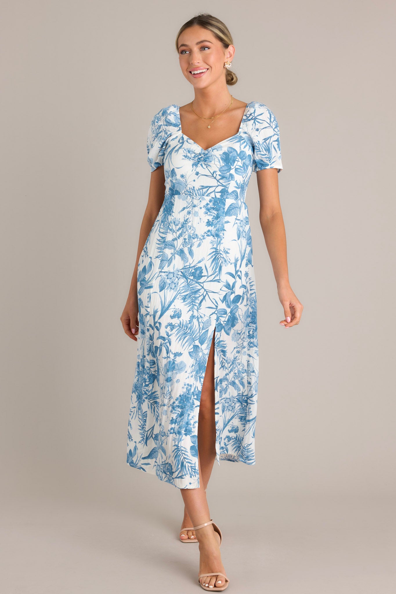Elegant blue floral midi dress with short puff sleeves, a sweetheart neckline, a fitted bodice, a cinched waist, and a mid-length skirt with a front slit.