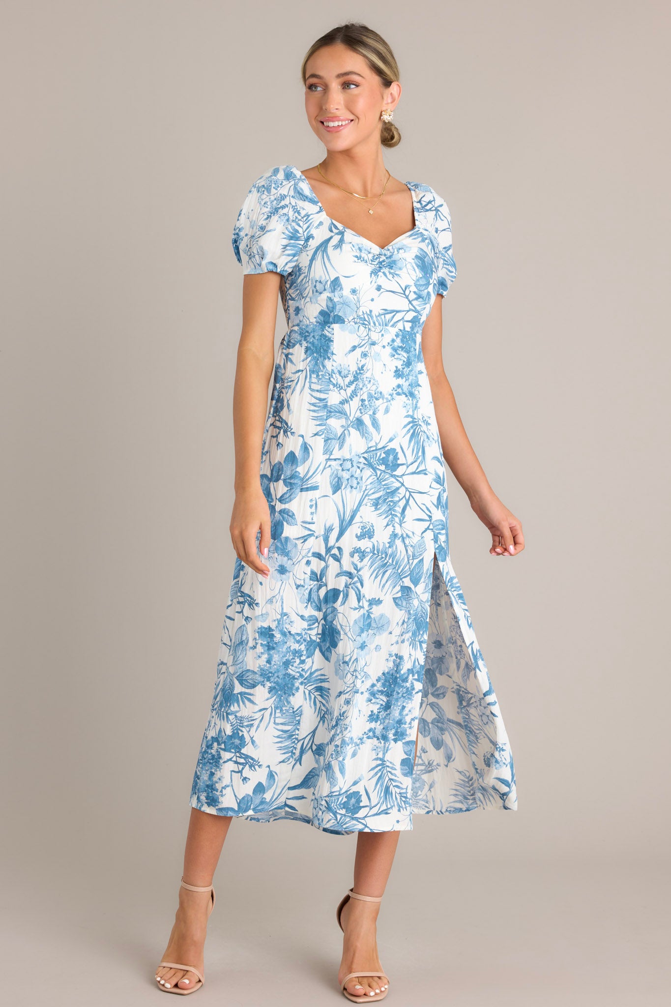 Blue floral midi dress with a sweetheart neckline, short puff sleeves, fitted bodice, cinched waist, and a mid-length skirt with a front slit.