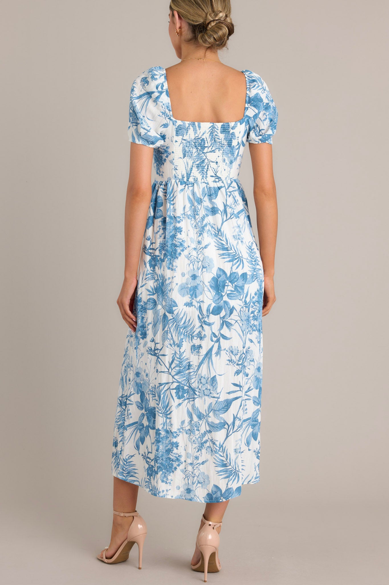 Back view of this blue floral midi dress featuring short puff sleeves, a fitted bodice, cinched waist, and a mid-length skirt with a blue botanical print.