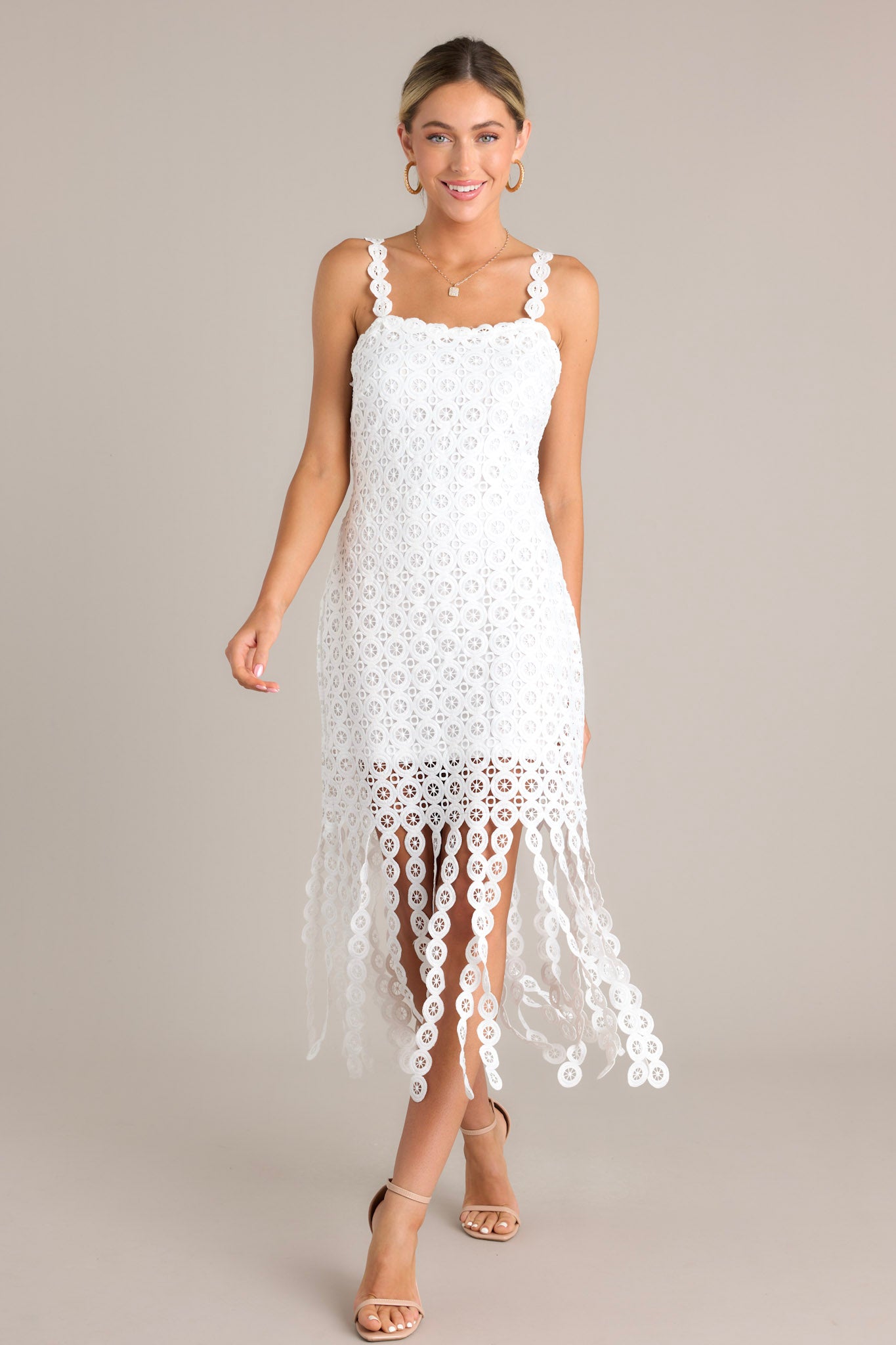 Action shot of a white midi dress with a square neckline, detailed adjustable straps, a discrete side zipper, a unique lace pattern, and detailed hanging fringe, highlighting the dress's flow and movement.