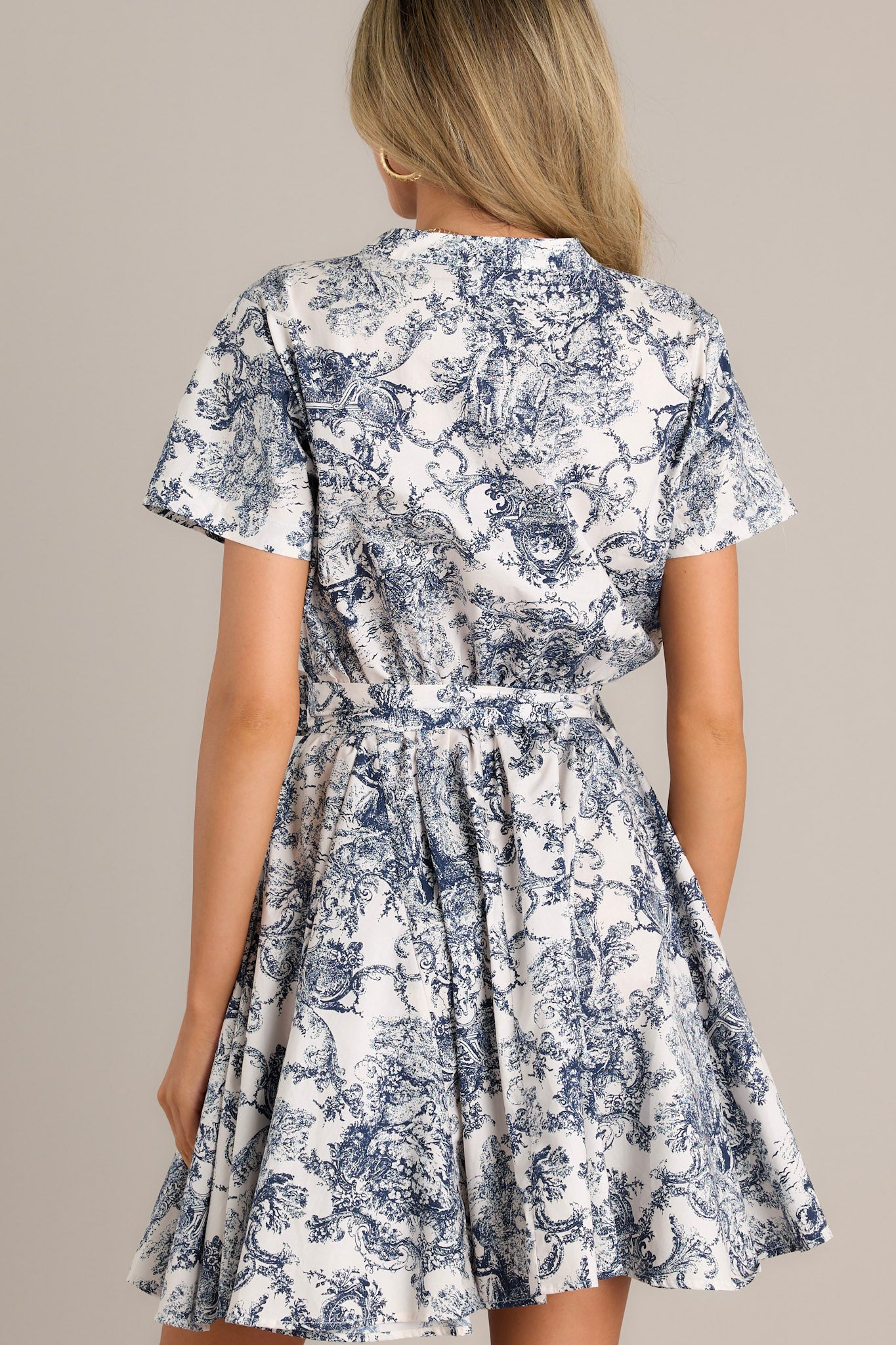 Front view of a navy mini dress featuring a v-neckline, a button front bodice, an elastic waistband, a self-tie waist belt, belt loops, short sleeves, and a flowing silhouette.