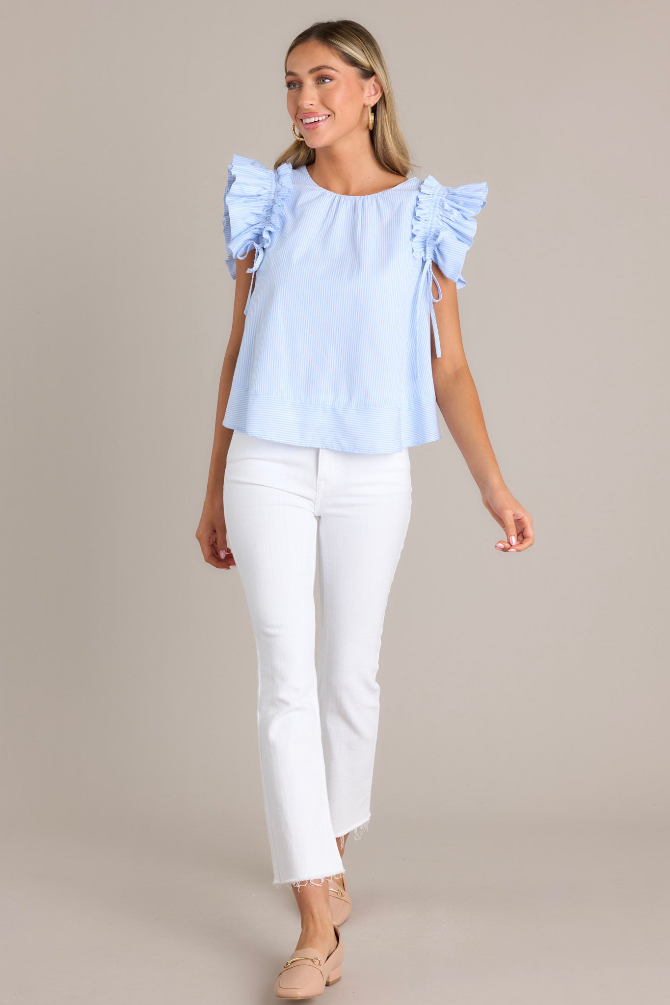 This blue stripe top features a relaxed fit, a crew neckline, vertical stripes, and layered ruffle sleeves with adjustable bows for a custom fit.