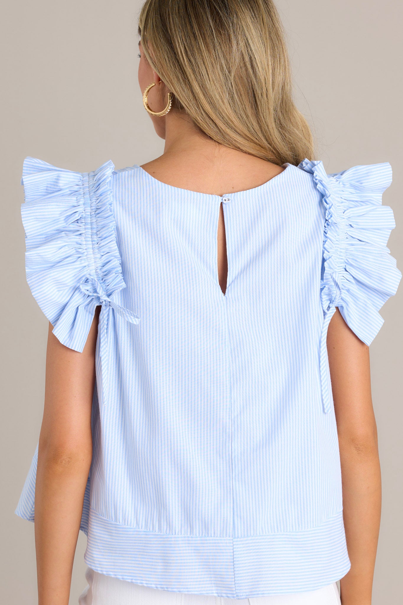 Back view of this blue stripe top featuring a relaxed fit, crew neckline, vertical stripes, and layered ruffle sleeves with adjustable bows.