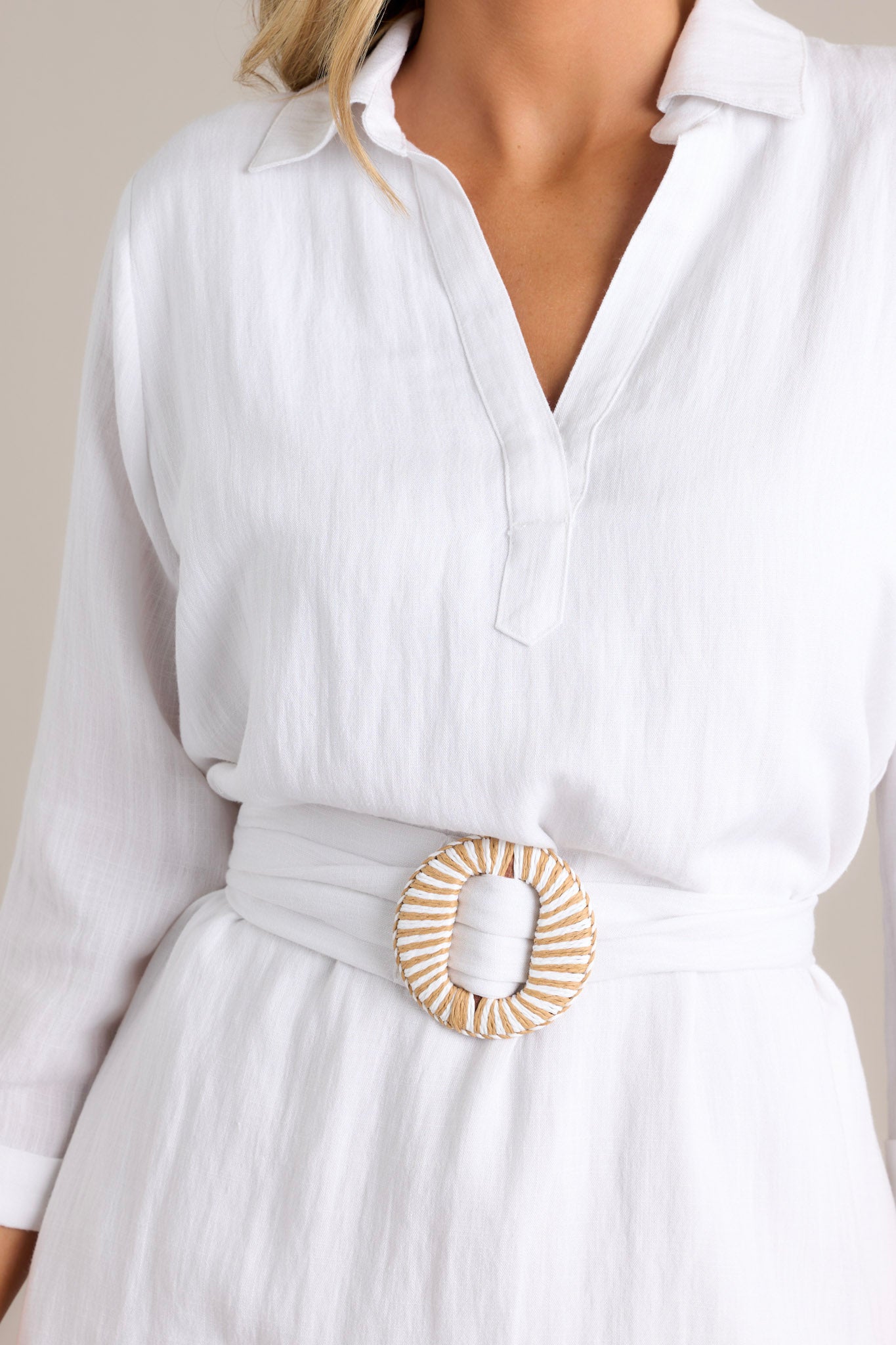 Close-up of the fabric and belted waist with a decorative buckle on a white shirt dress with three-quarter sleeves.