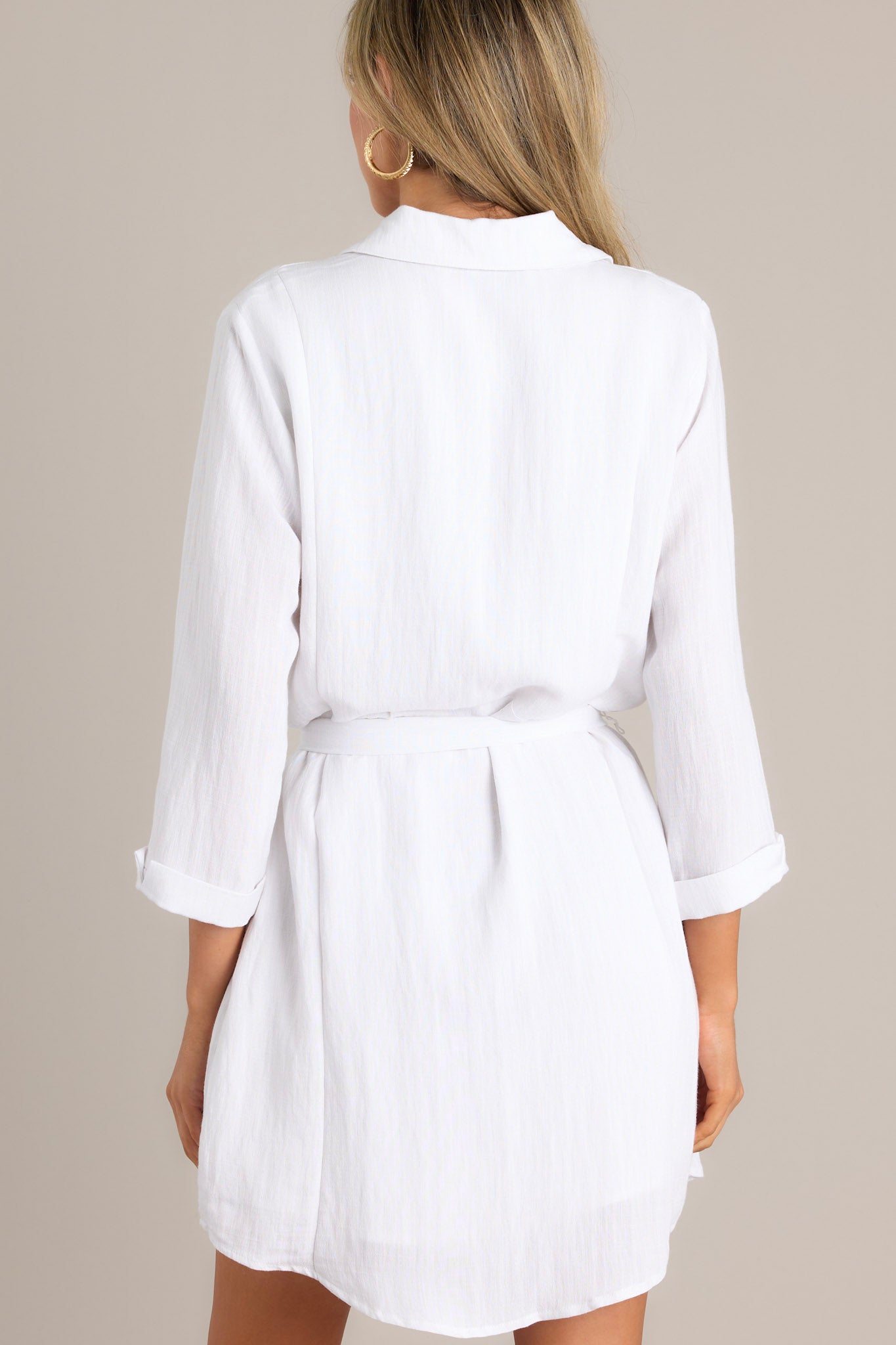 Back view of a white shirt dress with a belted waist and three-quarter sleeves, highlighting the dress's clean lines and simple elegance.