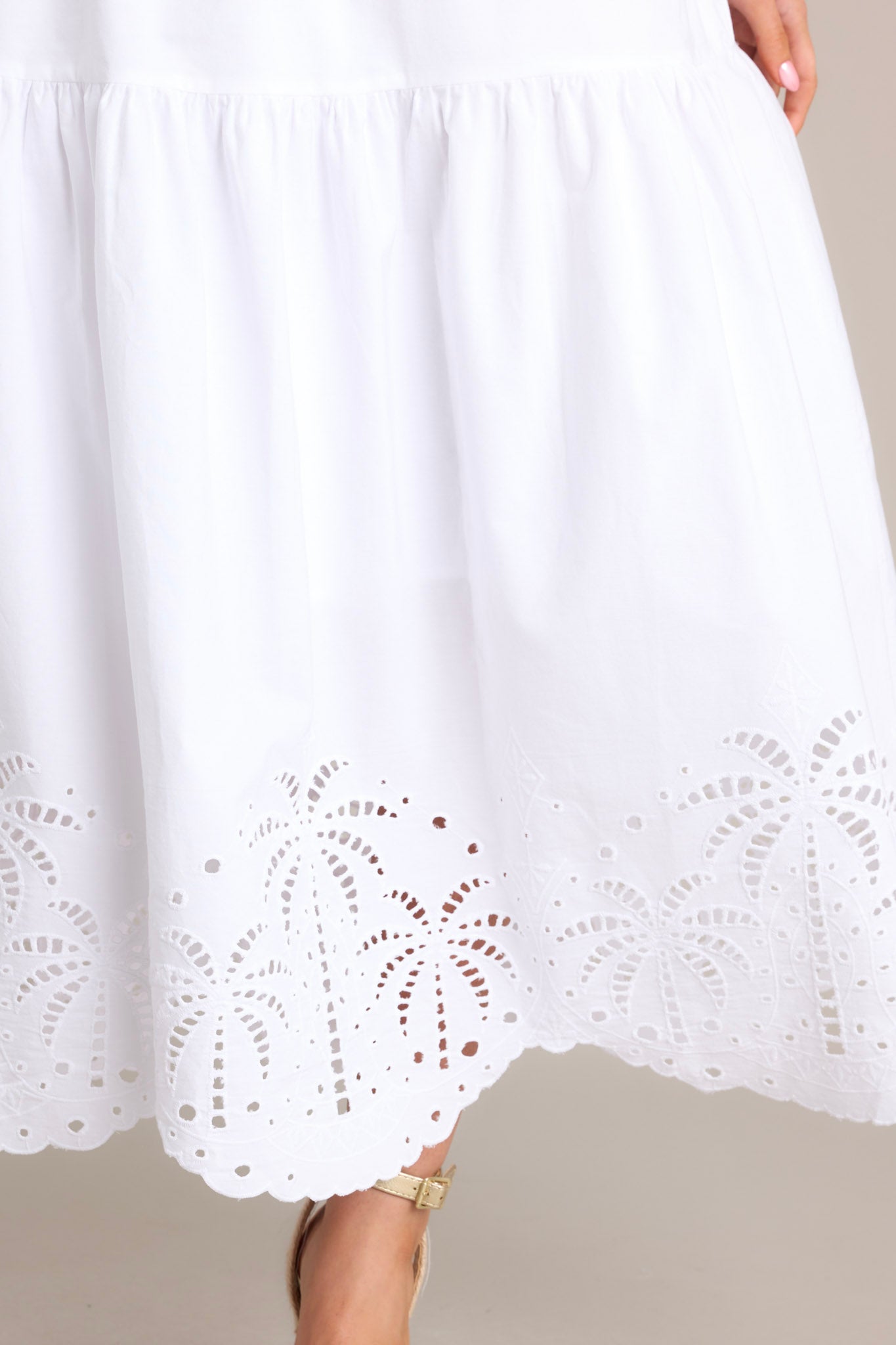 Close up view of the detailing on the bottom of this white midi that features an elastic square neckline, thick adjustable straps, a thick waistband with a self-tie back feature.