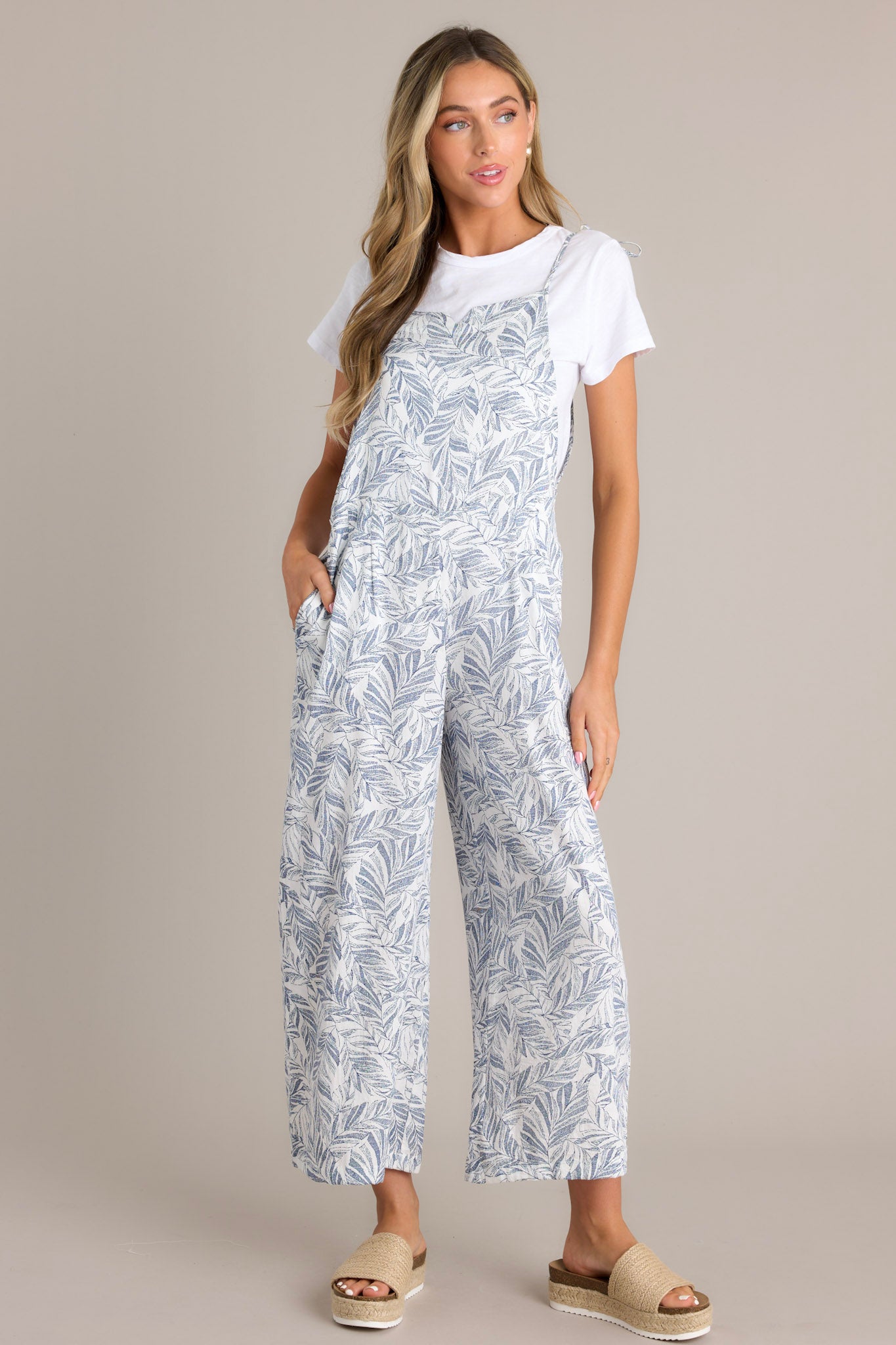 Casual jumpsuit featuring a light blue and white leaf print, wide legs, and adjustable tie straps.