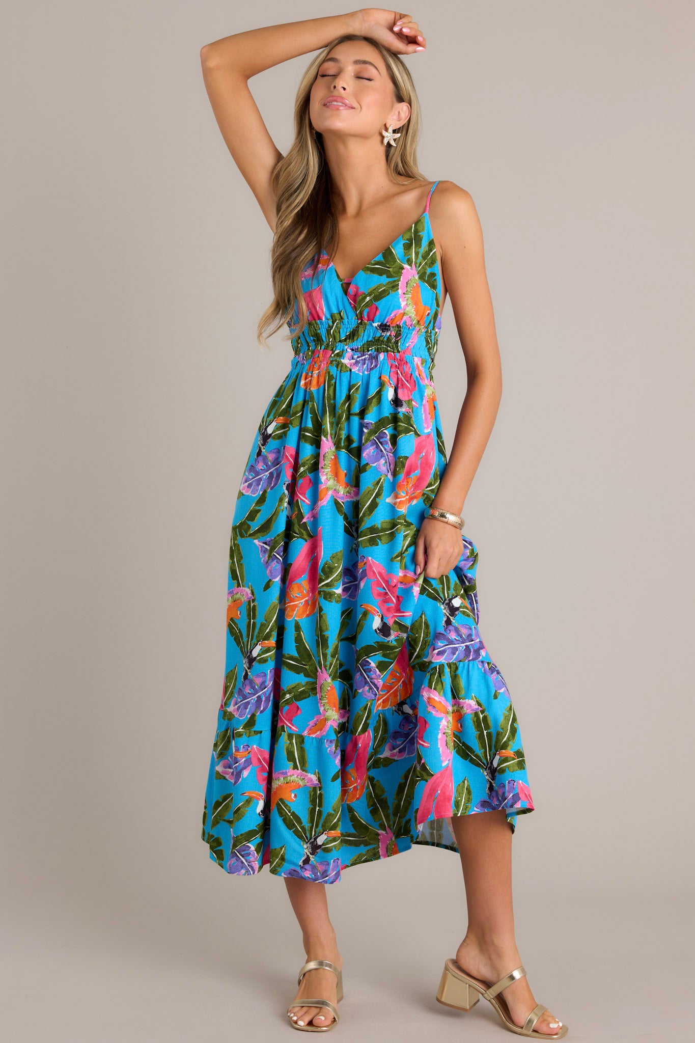 Action shot of a blue midi dress with a V-neckline, thin adjustable straps, an open back, smocked waistband, and a vibrant color scheme, highlighting the flowing silhouette.