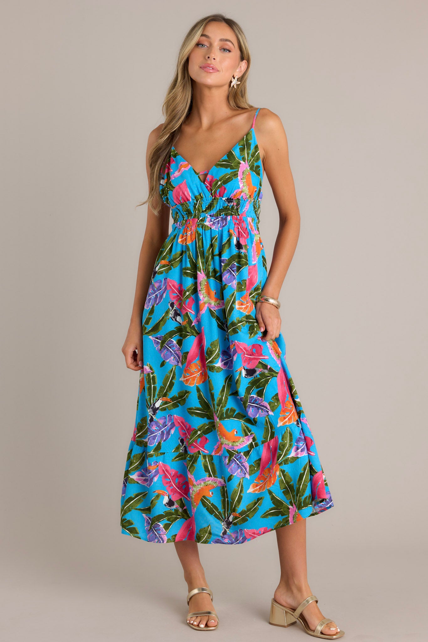 Front view of a blue midi dress featuring a V-neckline, thin adjustable straps, an open back, a fully smocked waistband, and a vibrant color scheme.