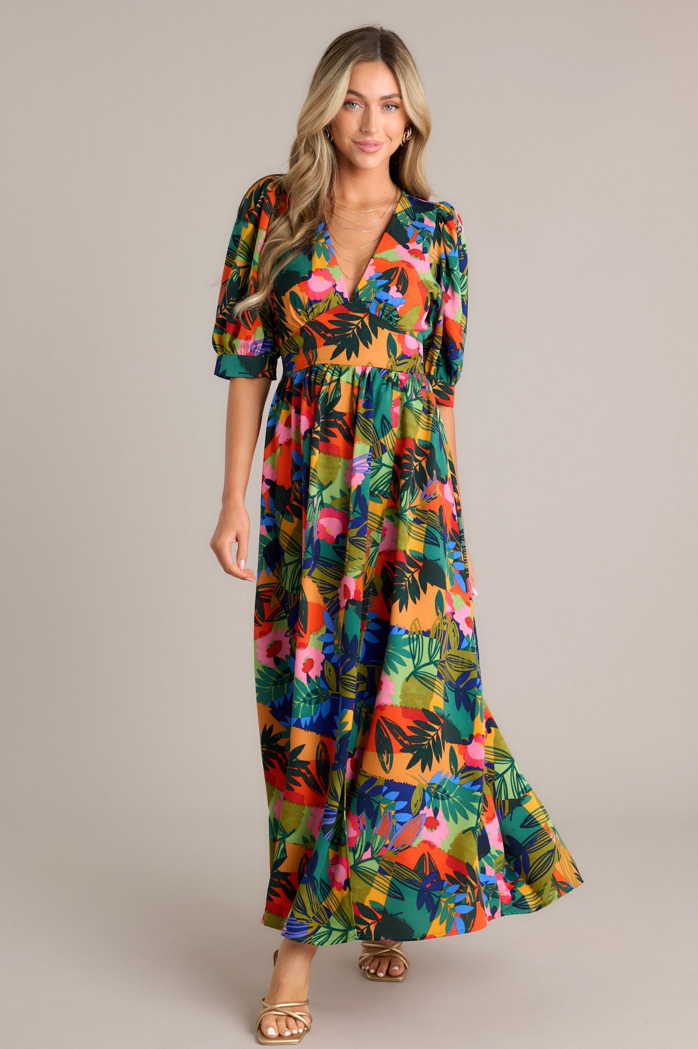 Full body view of this green multi maxi dress that features a plunging v-neckline, a keyhole with button closure in the back, and a thick waistband. 