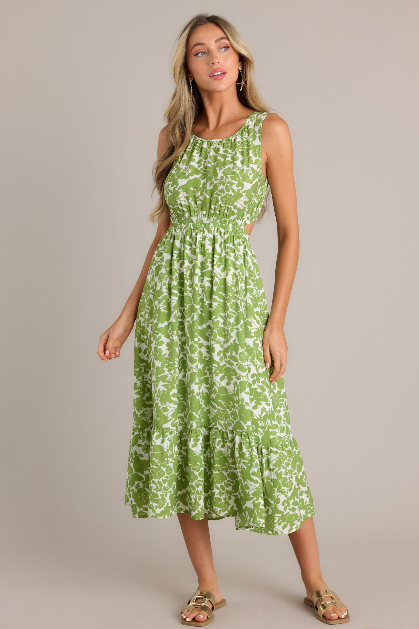 Full length view of a green and white floral print sleeveless dress with side cutouts, a gathered waist, and a tiered skirt, showcasing the elegant design.