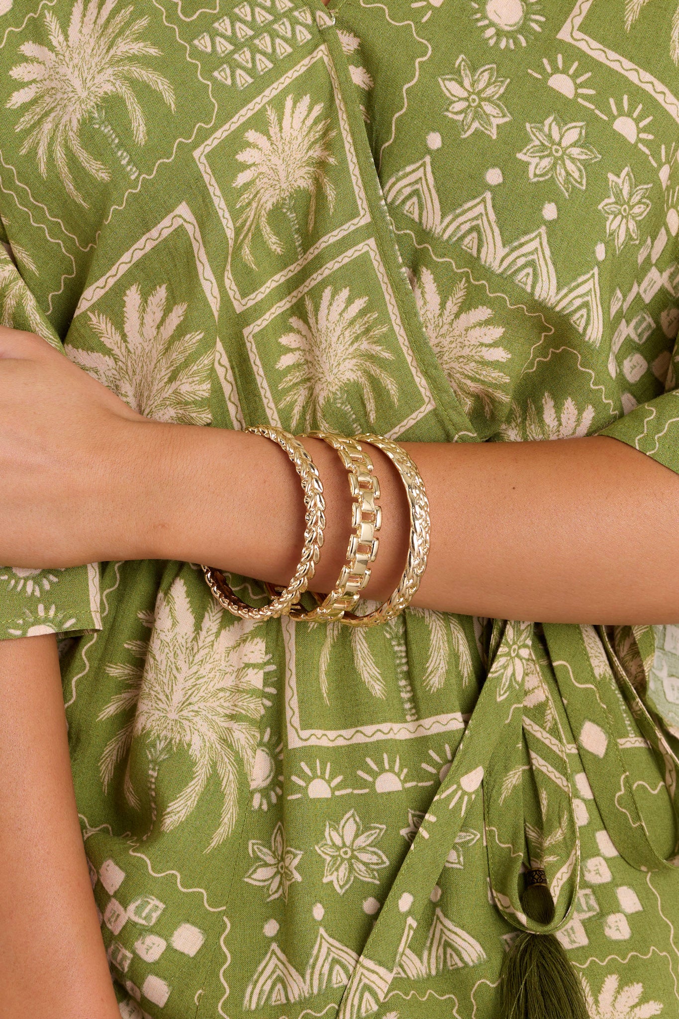 Close up view of these gold bangles that feature gold hardware, two bangles with a braided design, and one bangle with a chain-like design.