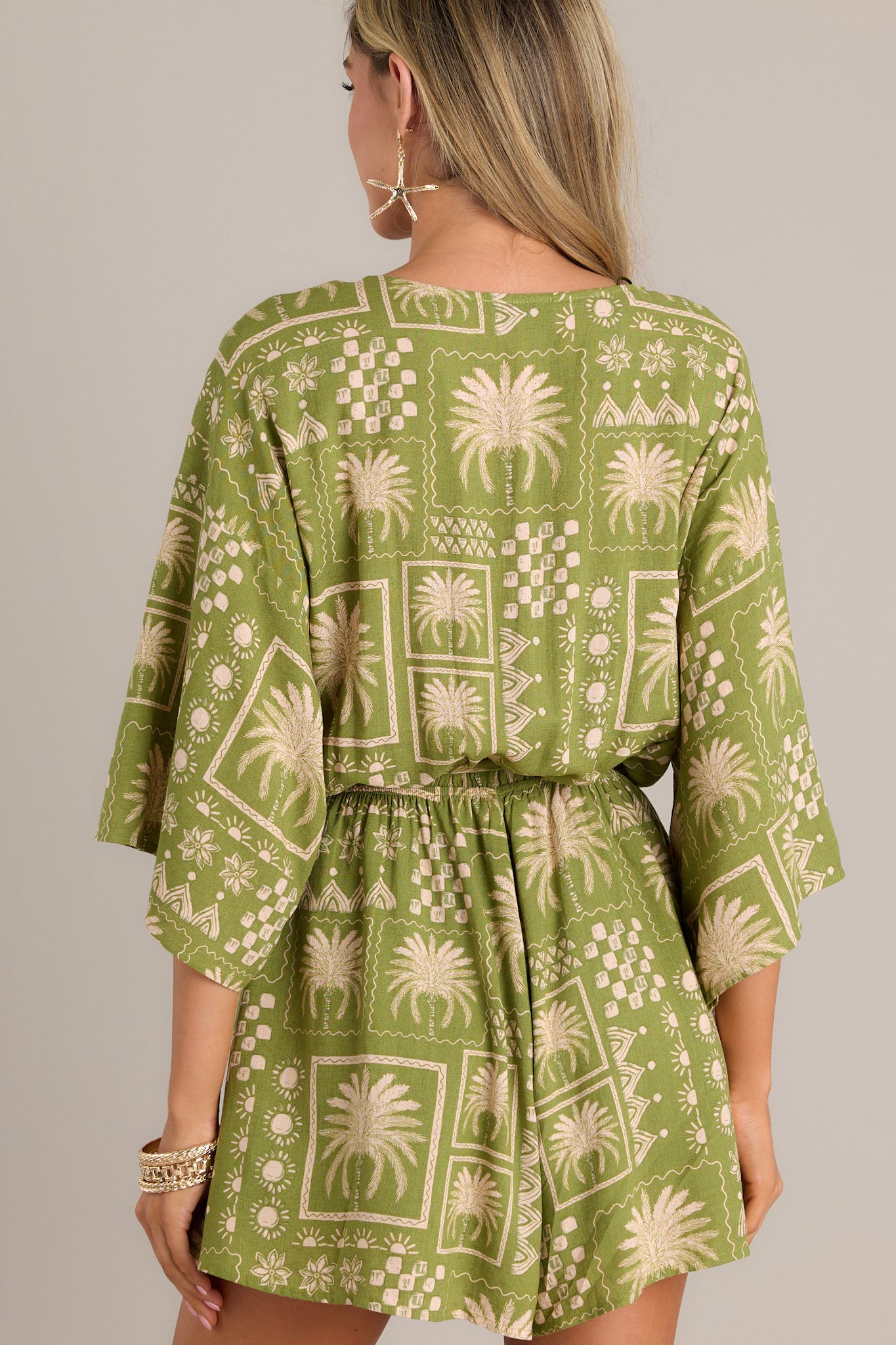 Back view of a green romper showcasing the elastic waistband, self-tie belt, and dolman sleeves.