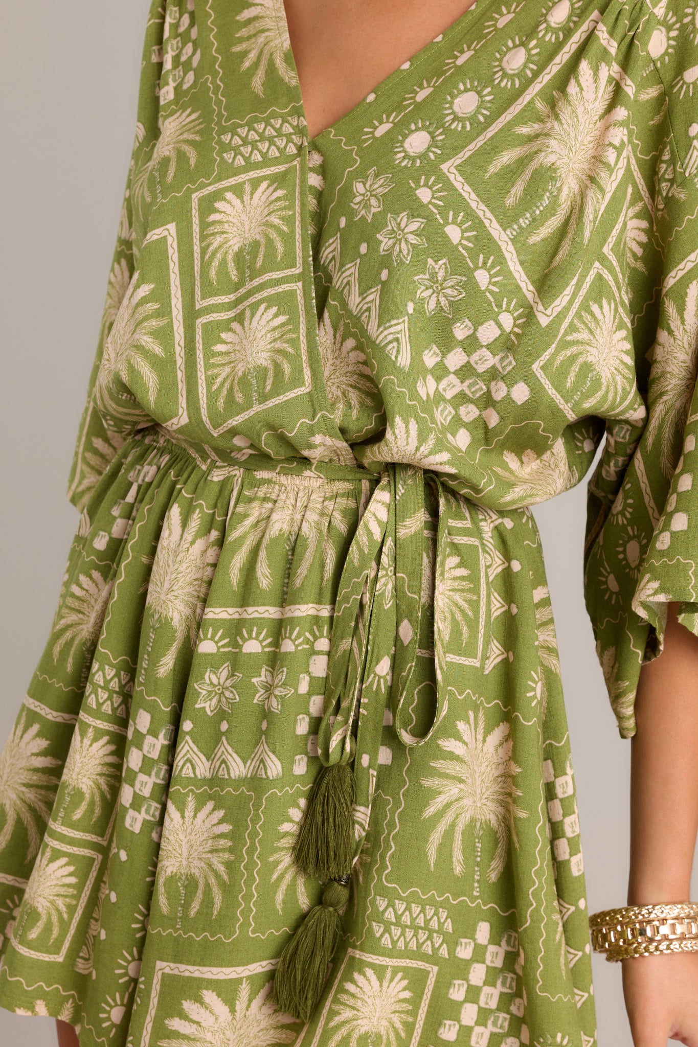 Close-up of the V-neckline, snap button closure, and self-tie belt on a green romper with quarter length dolman sleeves.