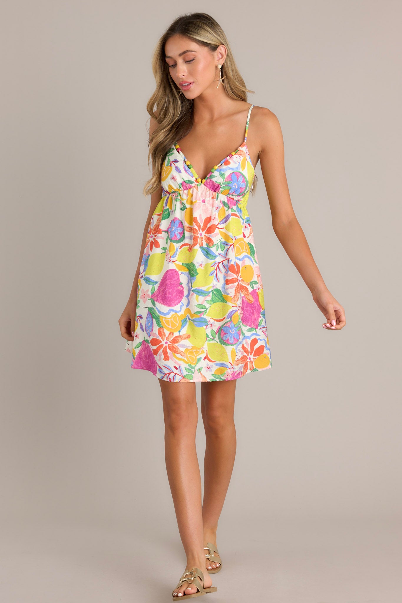 Front angled view of a floral mini dress featuring a beaded v-neckline, thin adjustable straps, a fitted lower bust, and a unique vibrant floral print.