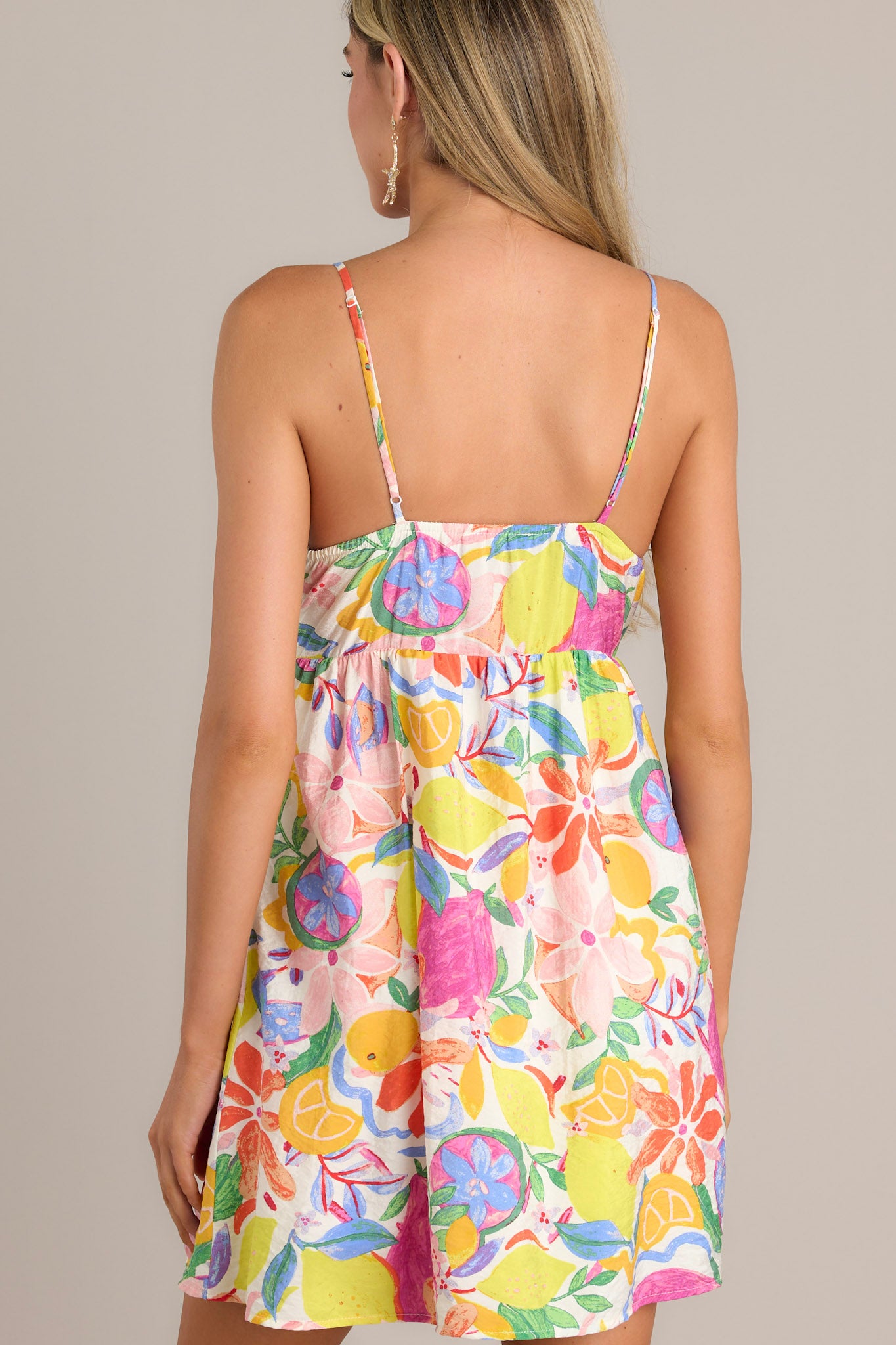 Back view of a floral mini dress highlighting the thin adjustable straps, a fitted lower bust, and a unique vibrant floral print.