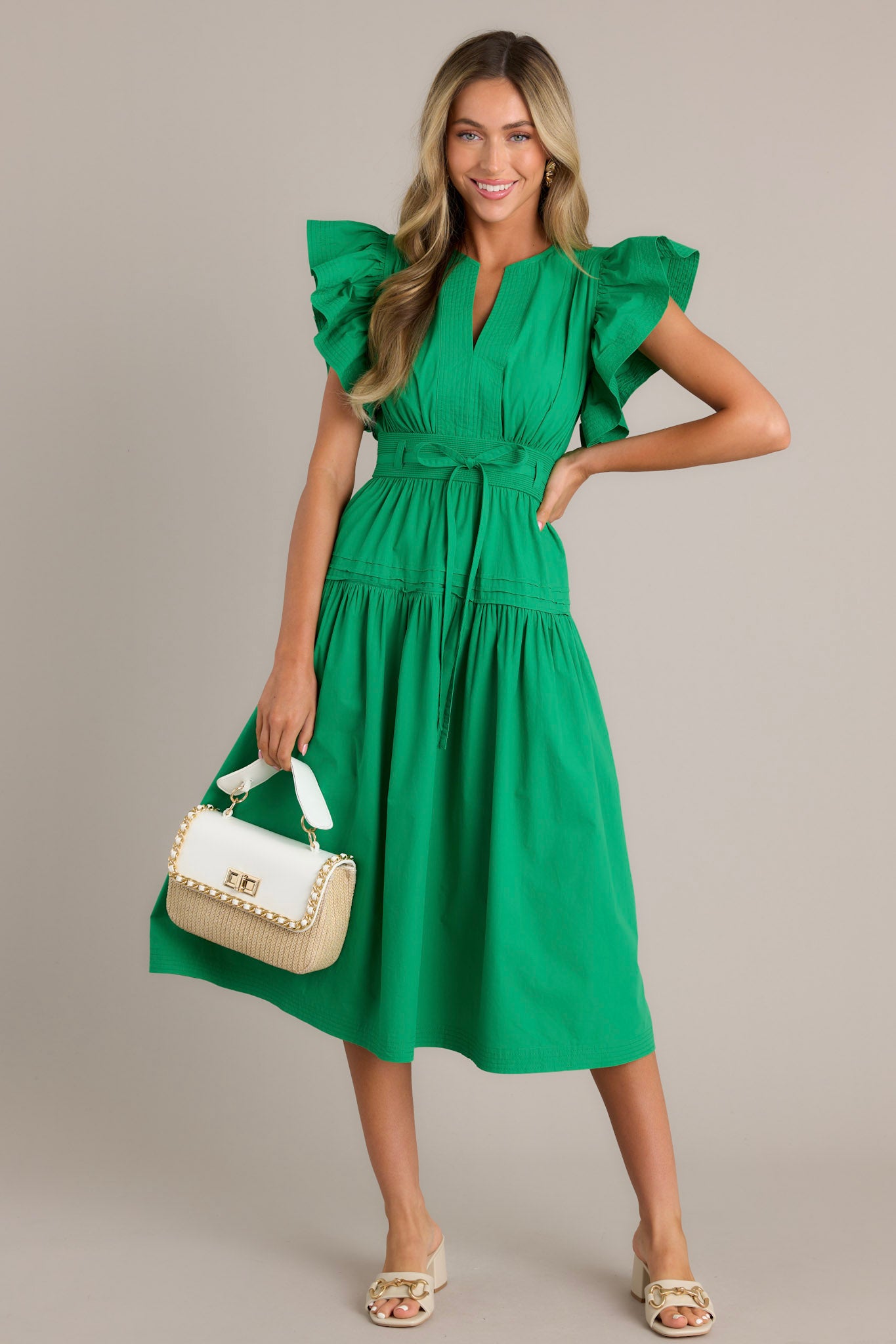 This green midi dress features a v-neckline, subtle chest pleats, a discrete side zipper, a thick waistband with a self-tie belt, a smocked waist insert, functional hip pockets, a single tier, and ruffled short sleeves.
