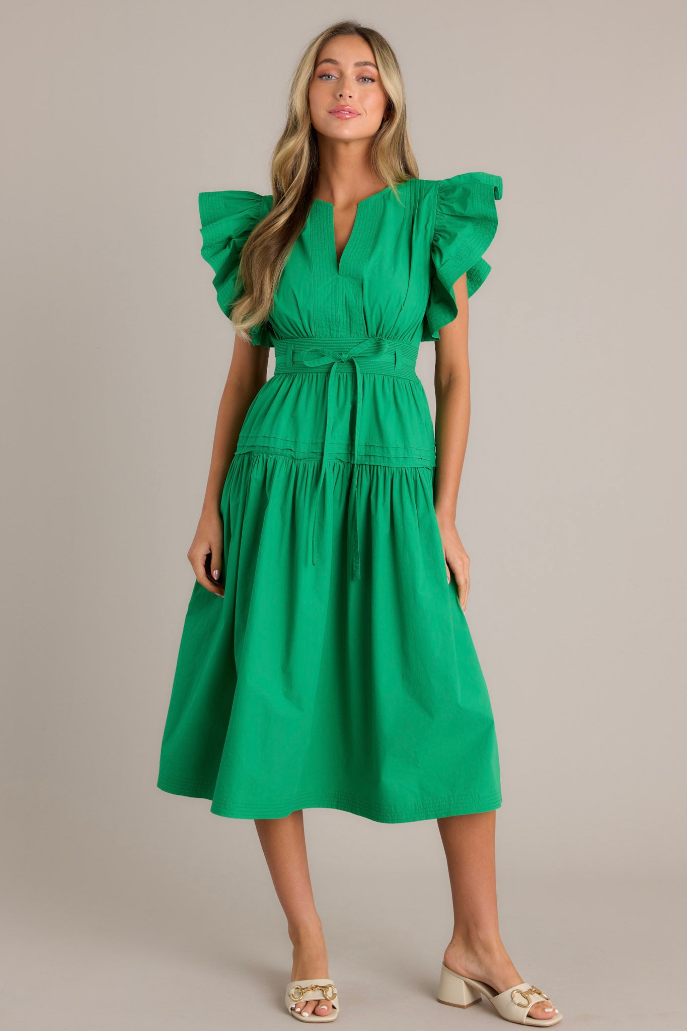 Front view of a green midi dress featuring a v-neckline, subtle chest pleats, a thick waistband with a self-tie belt, and ruffled short sleeves.