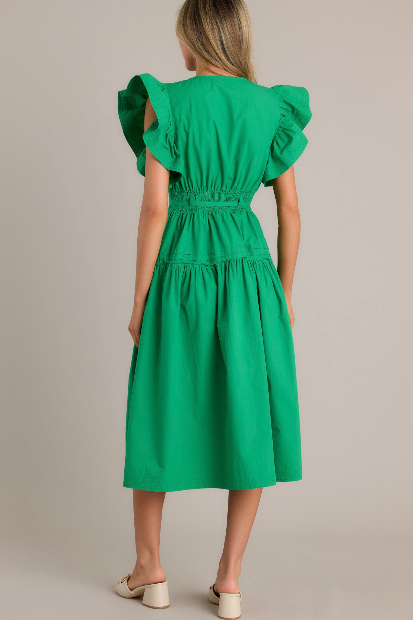 Back view of a green midi dress showcasing a smocked waist insert, functional hip pockets, and ruffled short sleeves.