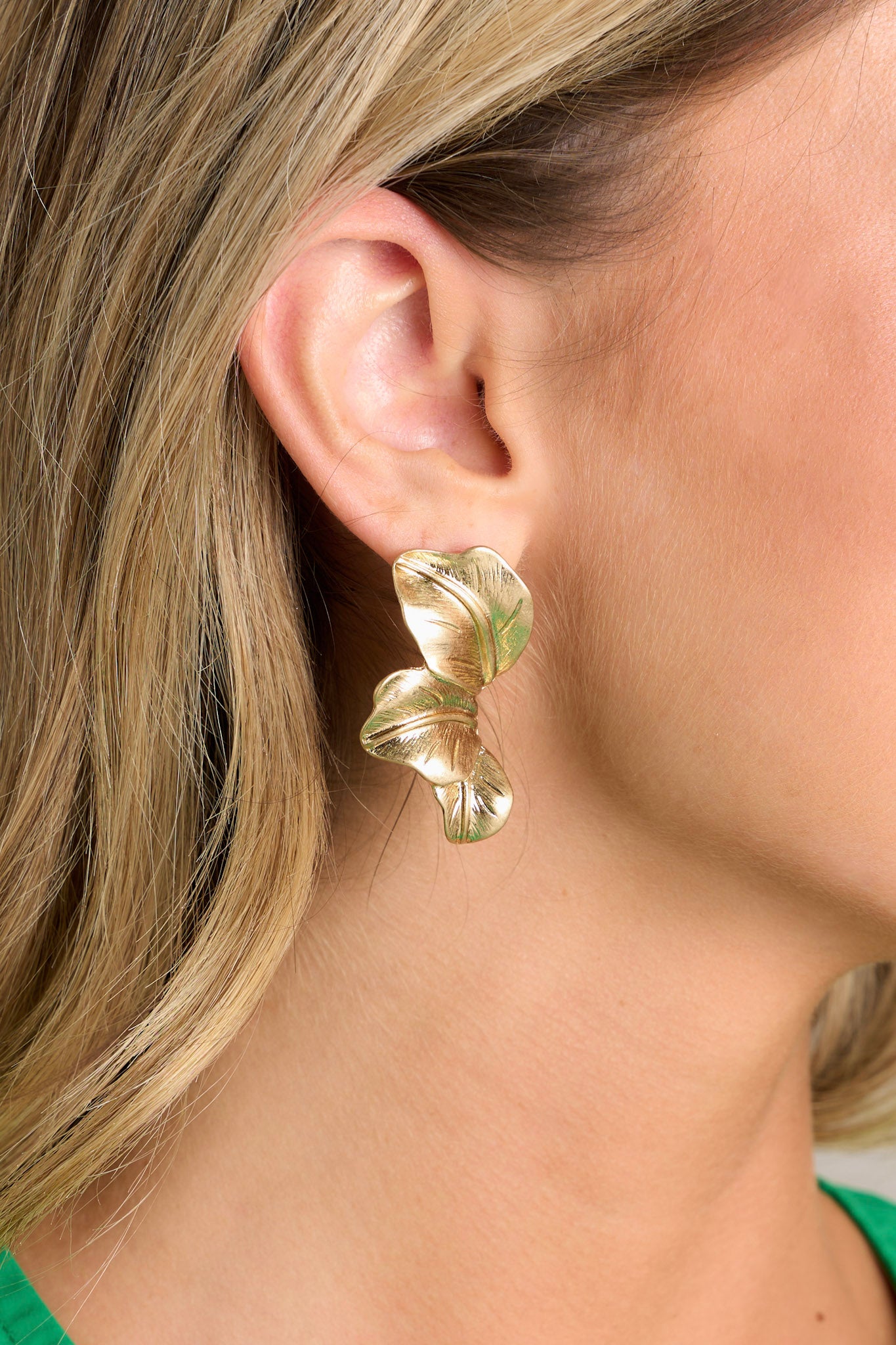 Close-up view of these gold earrings that feature a worn gold finish, three palm leaves, and secure post backings.