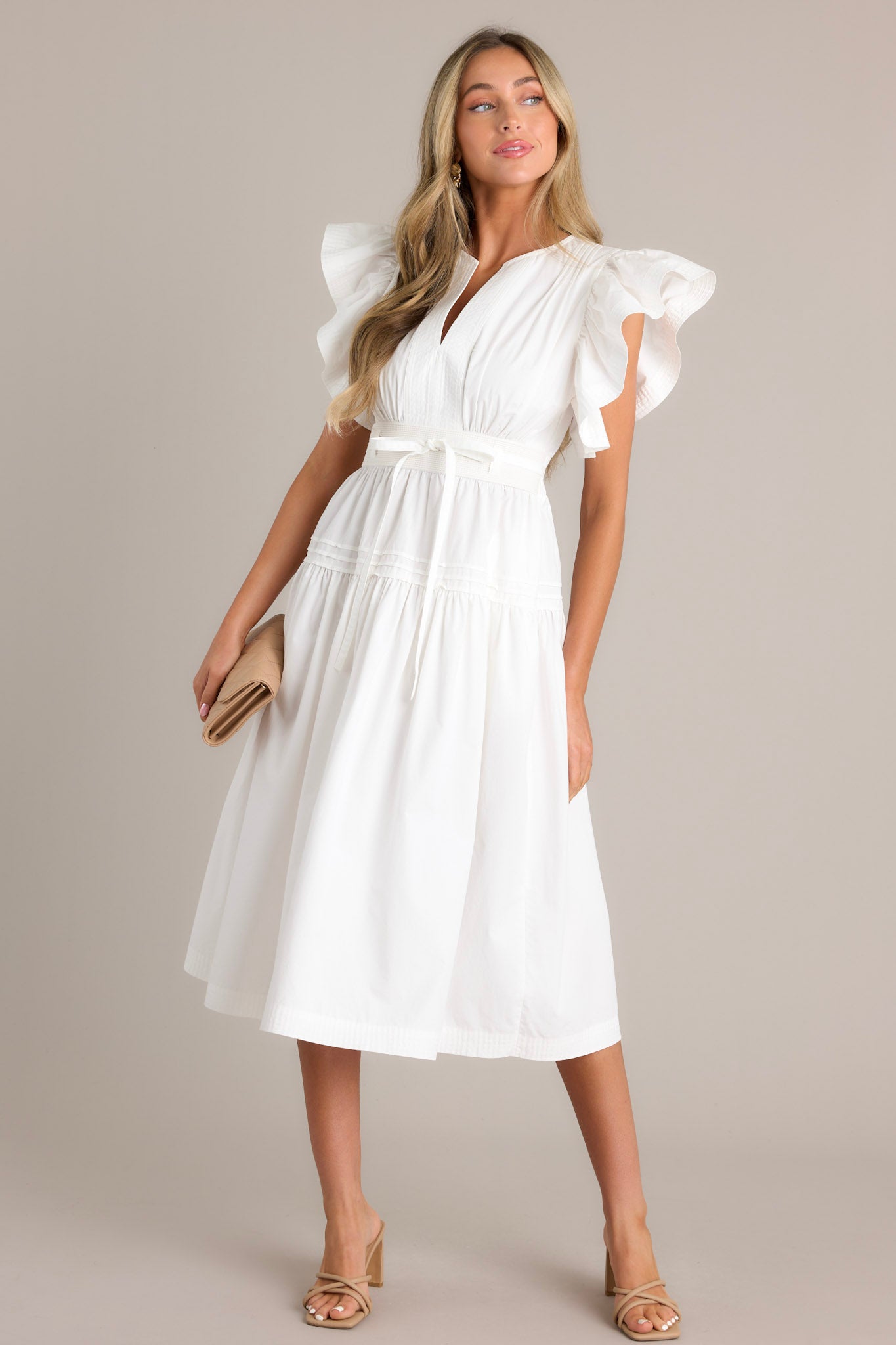 Full length view of a white midi dress with a v-neckline, subtle chest pleats, a discrete side zipper, a thick waistband with a self-tie belt, a smocked waist insert, functional hip pockets, a single tier, and ruffled short sleeves.