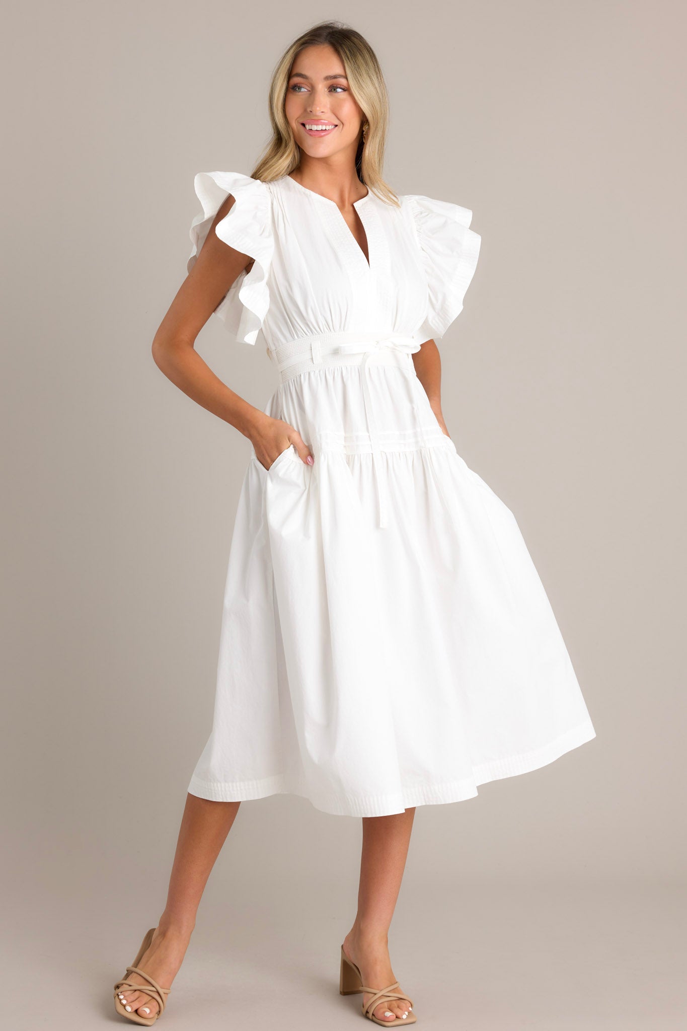 Action shot of a white midi dress highlighting the v-neckline, thick waistband with a self-tie belt, functional hip pockets, and ruffled short sleeves, showcasing the flow and movement of the dress.