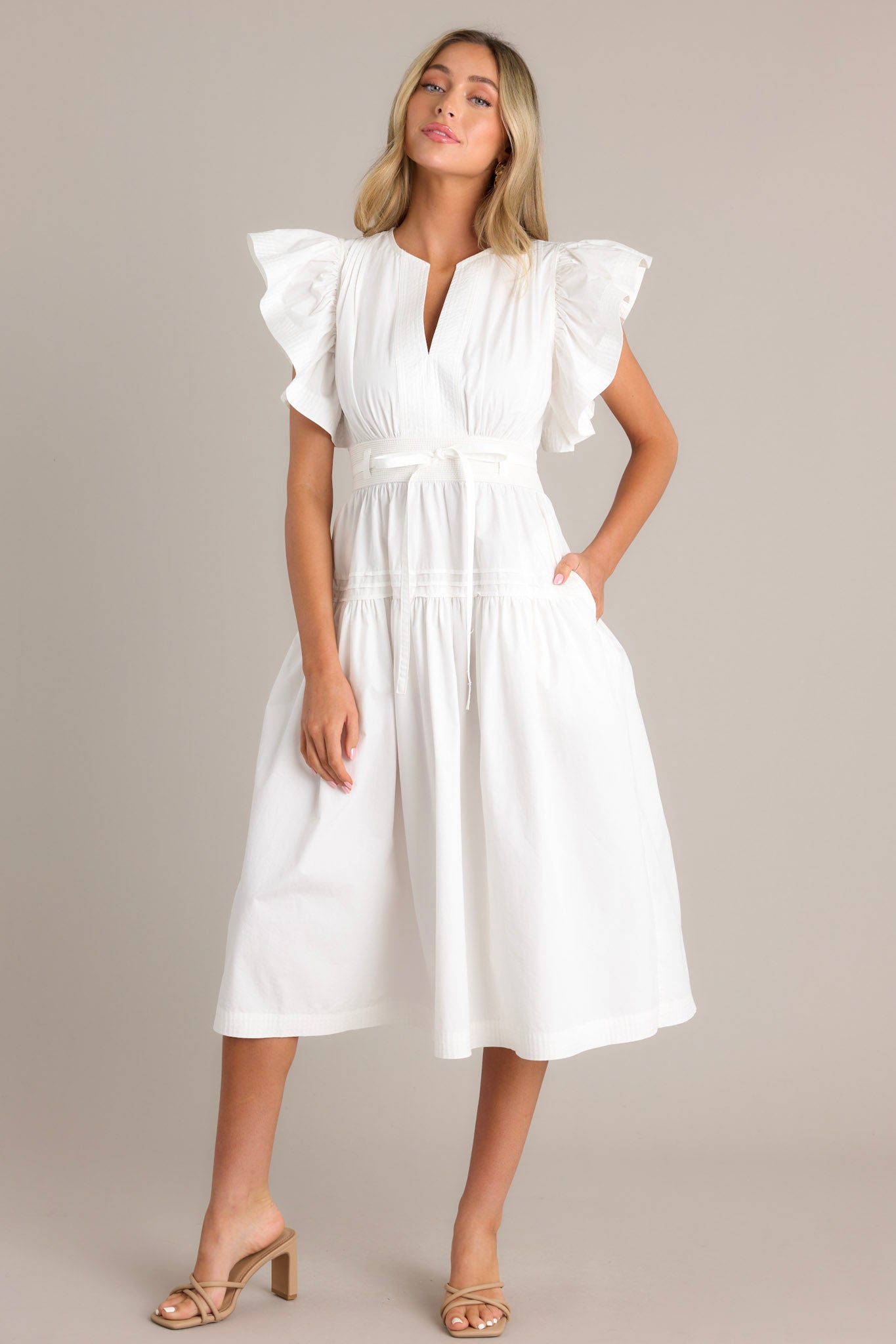 Front view of a white midi dress featuring a v-neckline, subtle chest pleats, a thick waistband with a self-tie belt, and ruffled short sleeves.