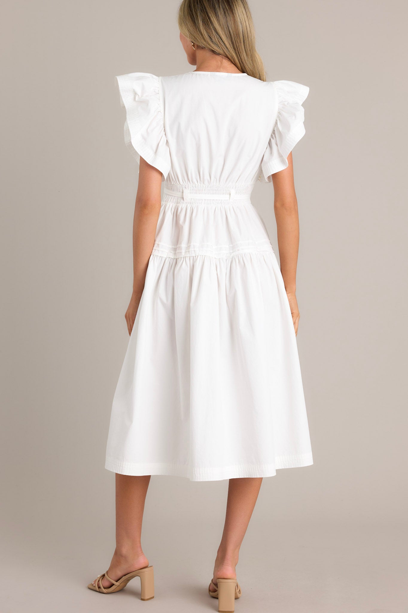 Back view of a white midi dress showcasing a smocked waist insert, functional hip pockets, and ruffled short sleeves.
