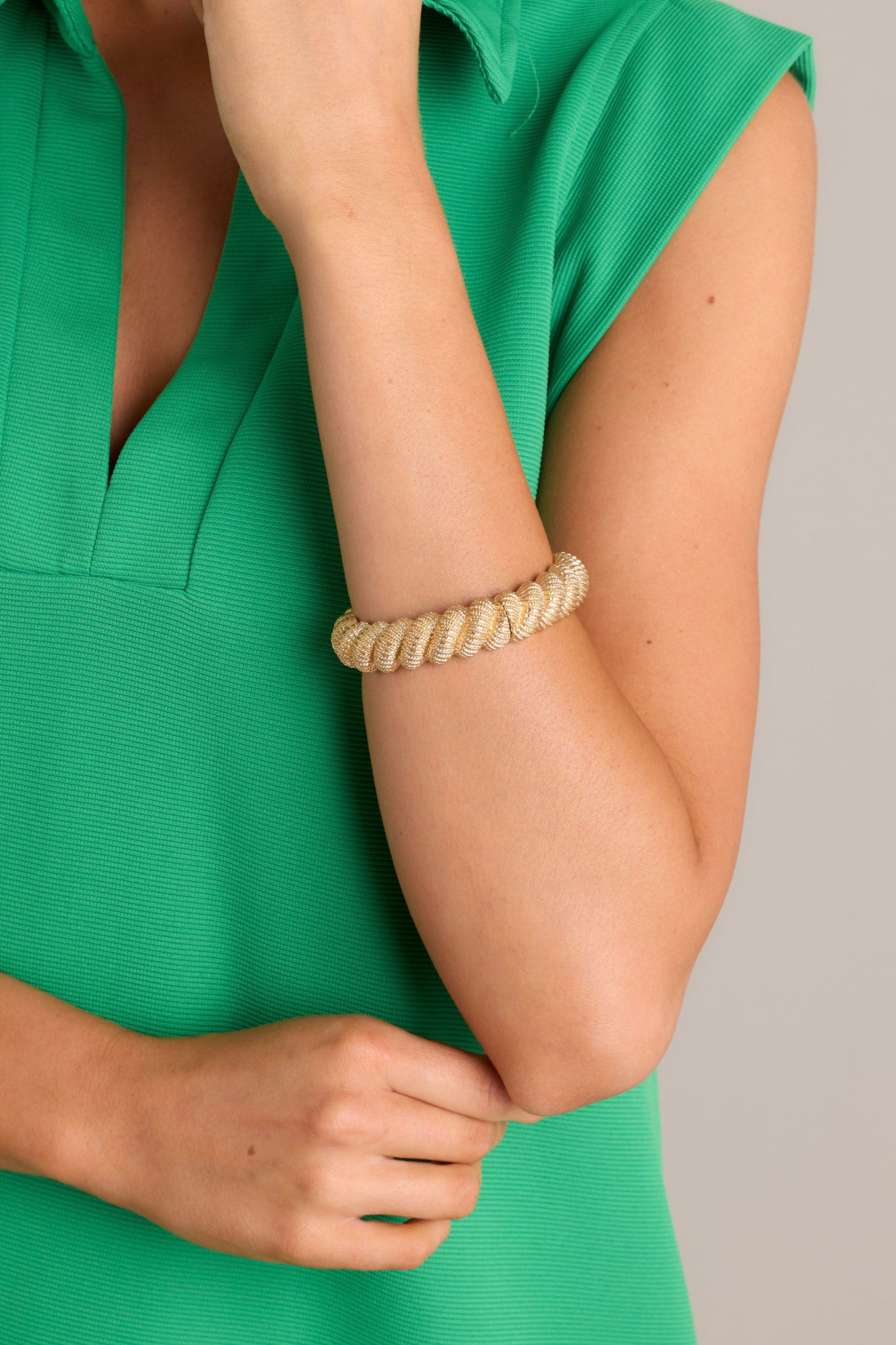 This gold bracelet features gold hardware, a textured rope design, and an elastic band underneath.