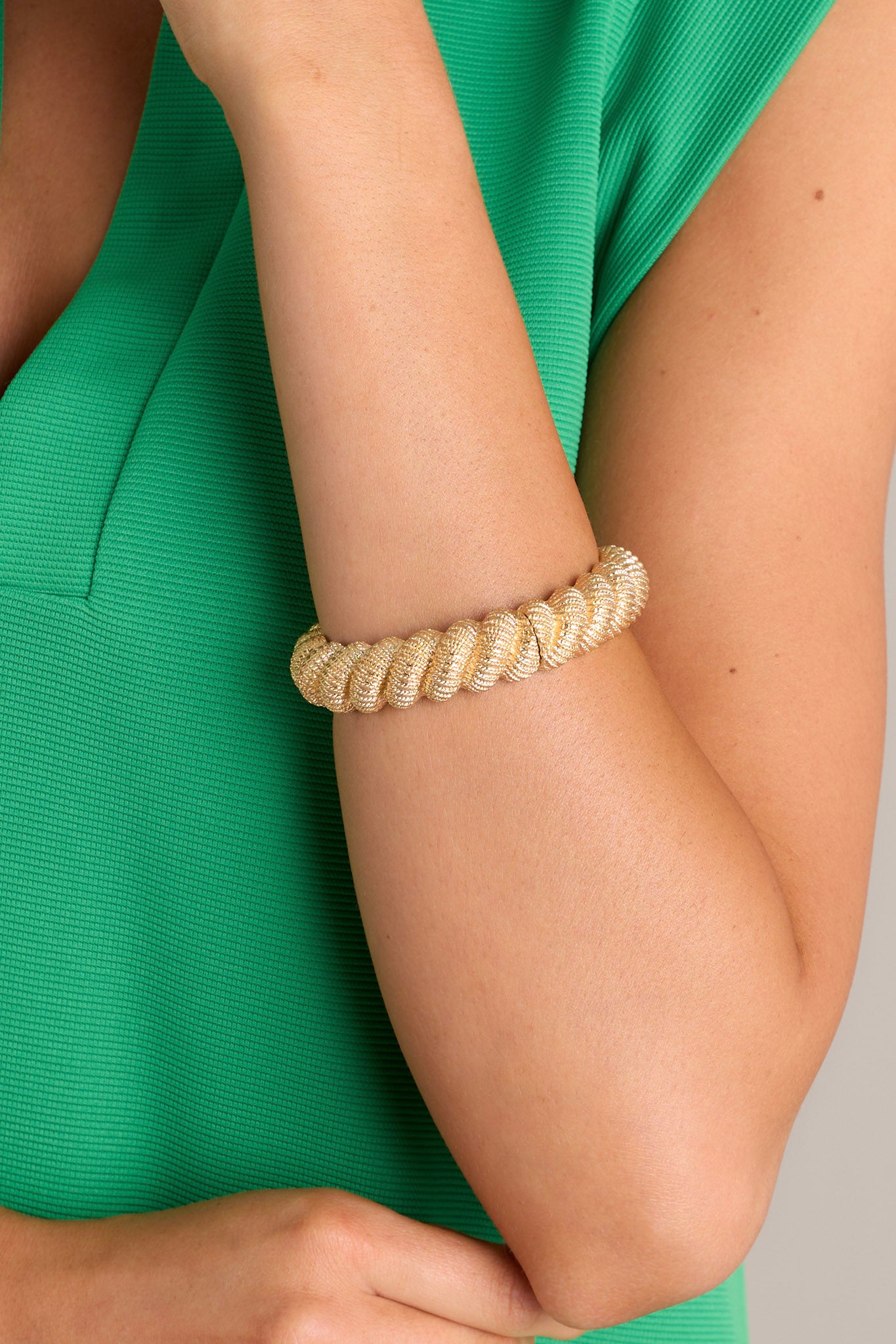 Close up view of this gold bracelet features gold hardware, a textured rope design, and an elastic band underneath.