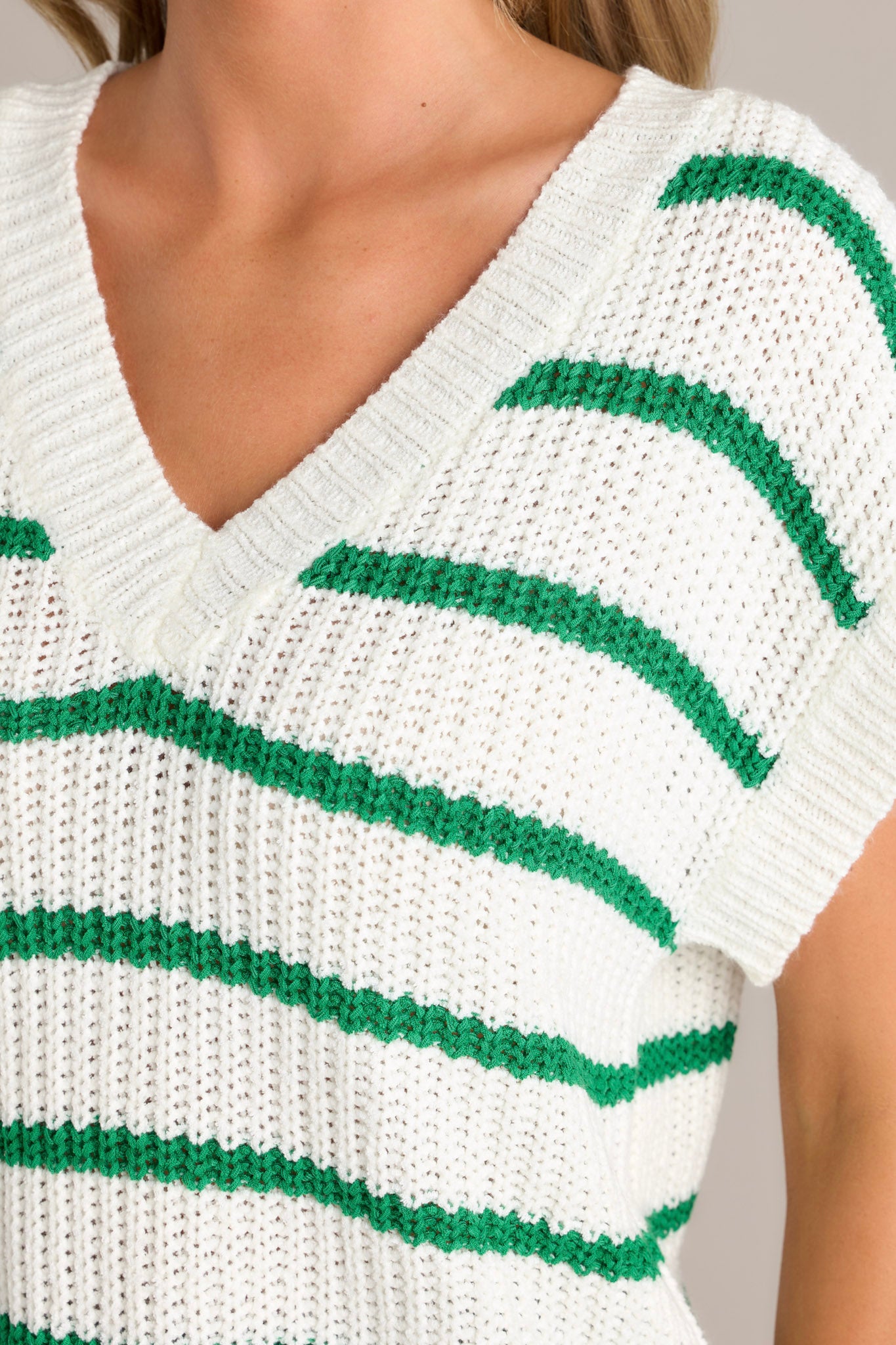 Close up view of this green stripe sweater top that features a ribbed v-neckline, a soft chunky knit material, horizontal stripes, a ribbed hemline, and ribbed short sleeves.