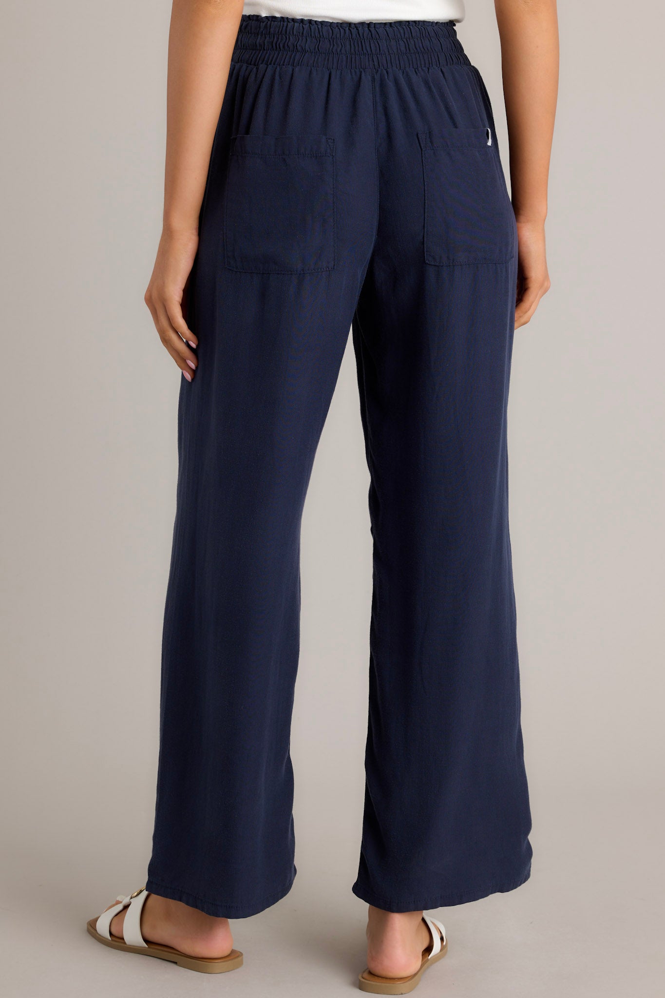 Back view of these Navy wide-leg pants with an elastic waistband and drawstring, paired with white sandals.