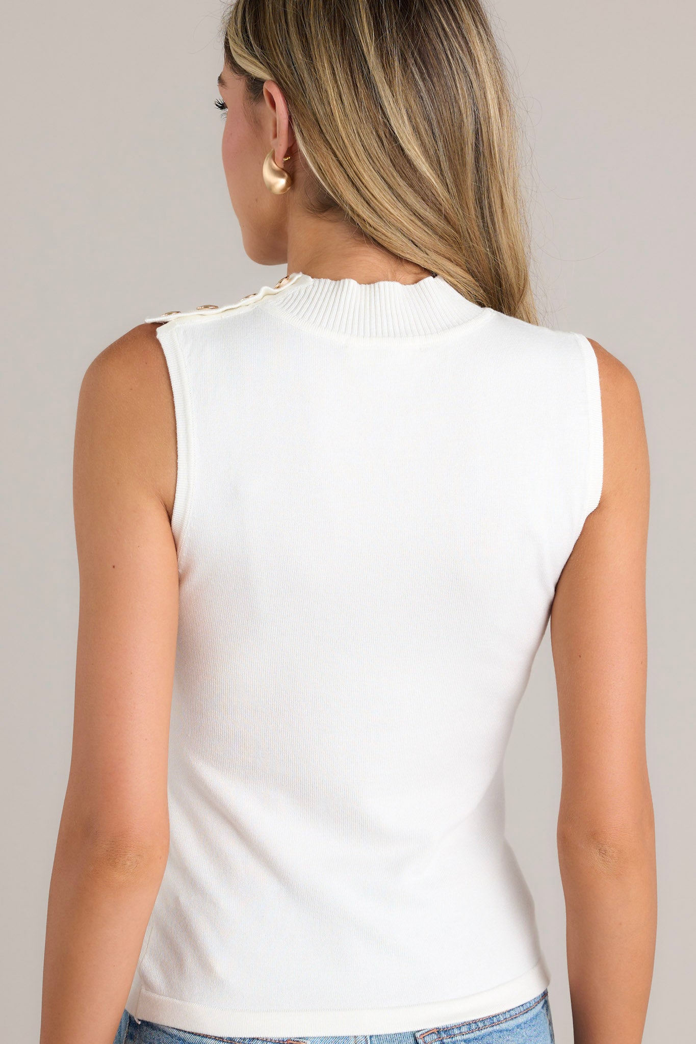 Back view of the material of this ivory tank that features a high ribbed neckline, 4 gold functional shoulder buttons, a fitted design, and a lightweight material.