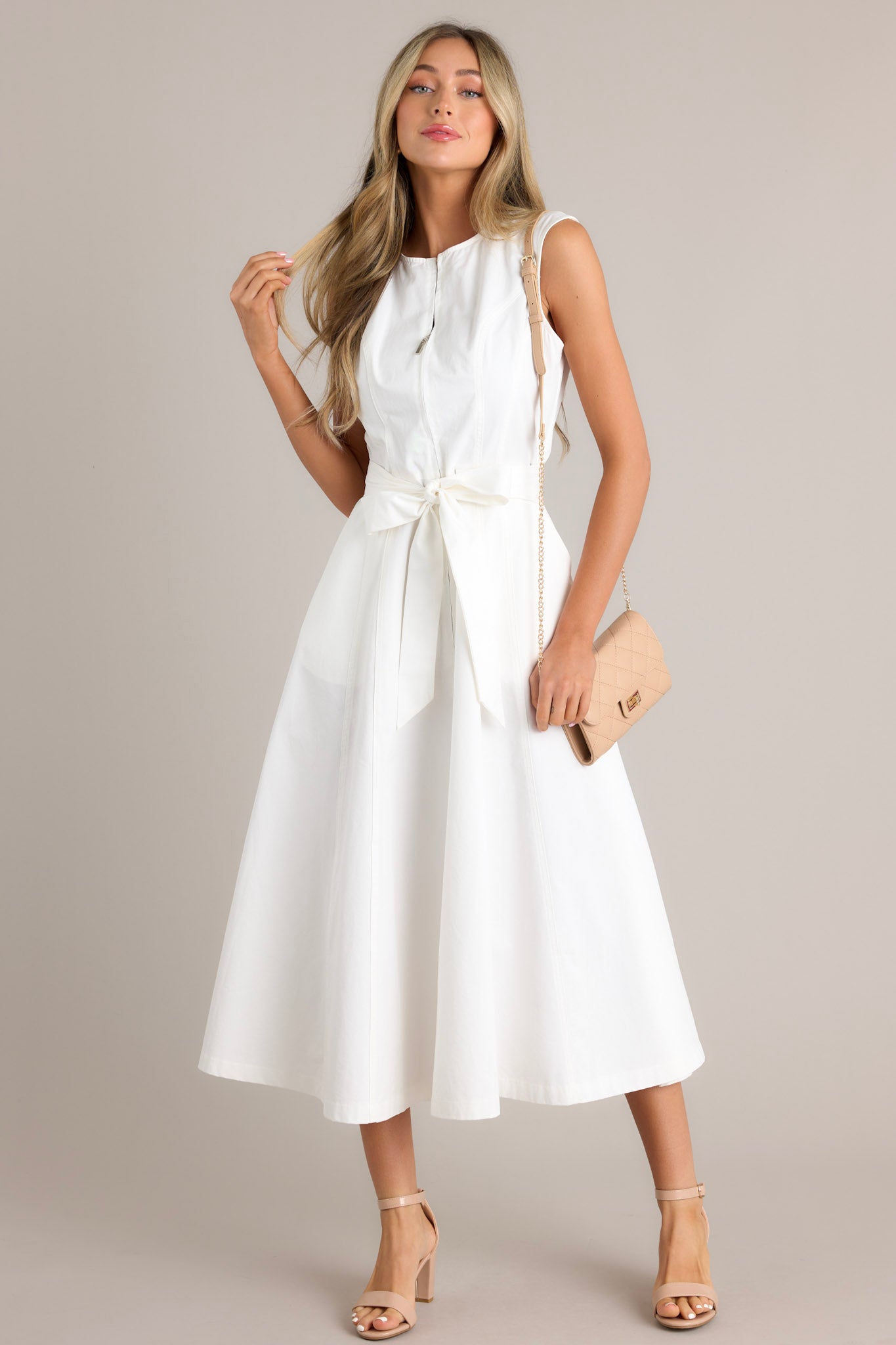 Front view of this white midi dress that features a round neckline, a zipper front, visible front & back seams, a self-tie waist belt, belt loops, functional hip pockets, and a flowing silhouette.