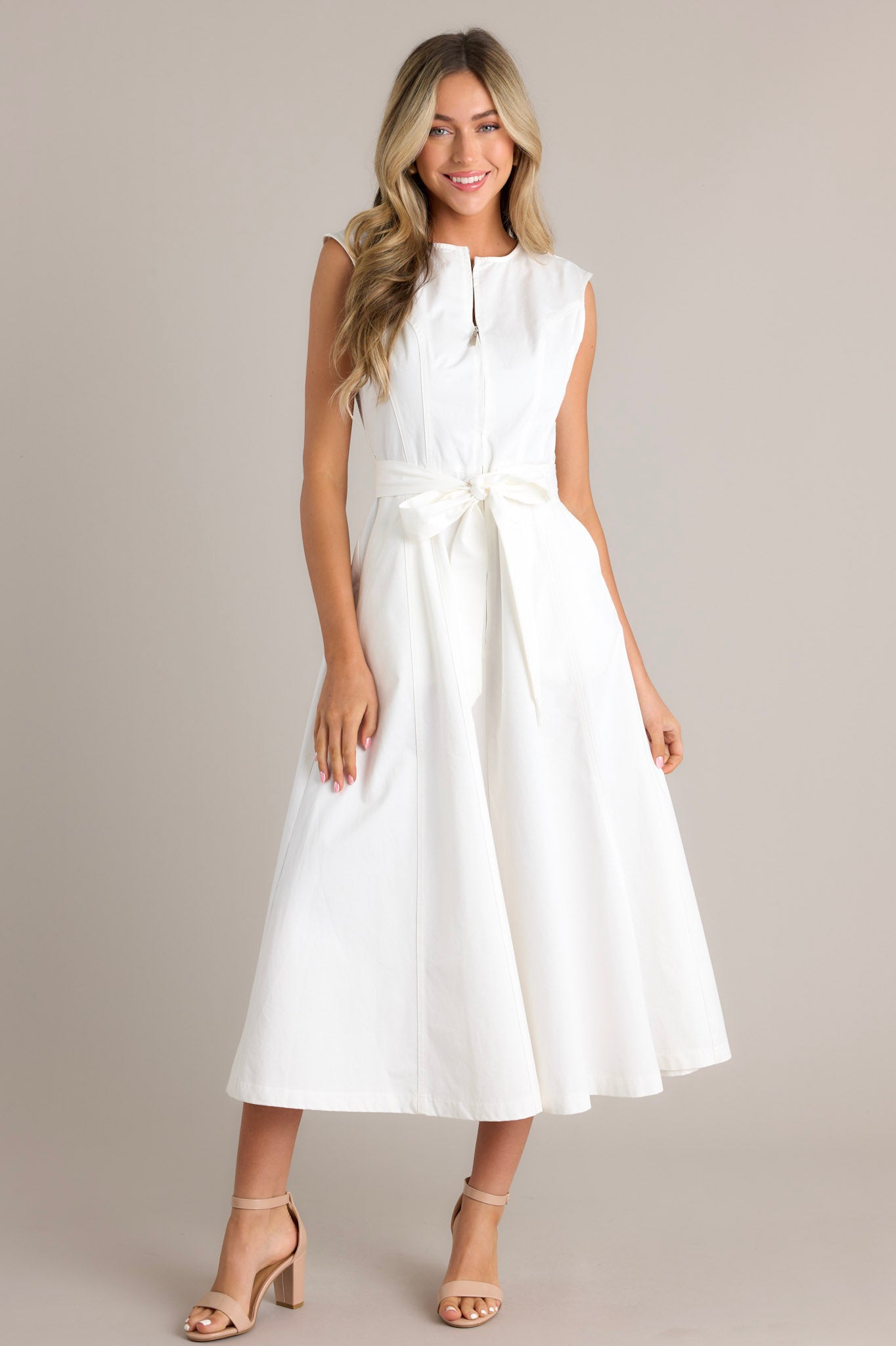 Sleeveless white dress with a flared skirt, front zipper closure, and a bow detail at the waist.