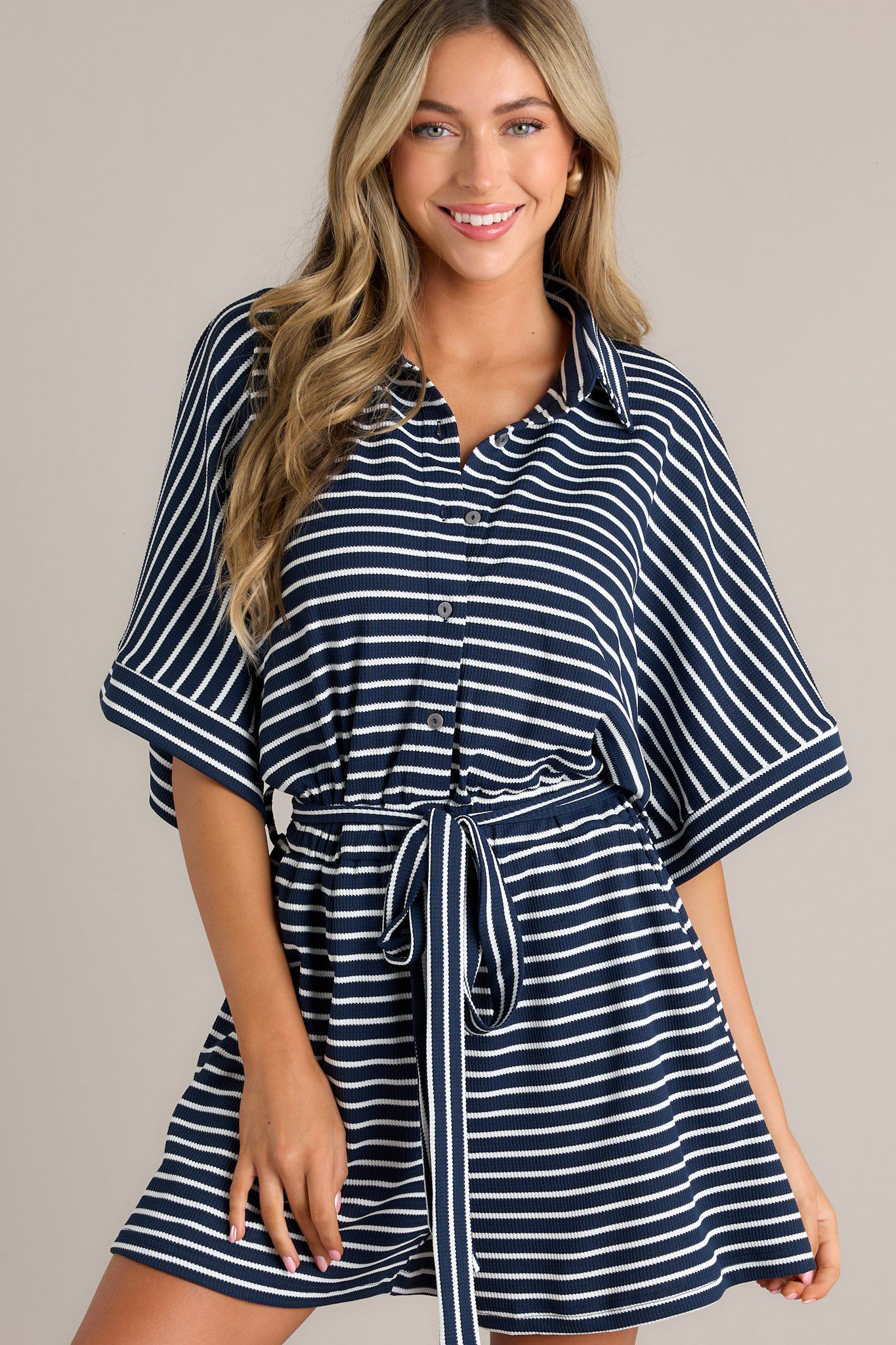 Front view of this navy blue and white striped romper with a front button closure and waist tie.