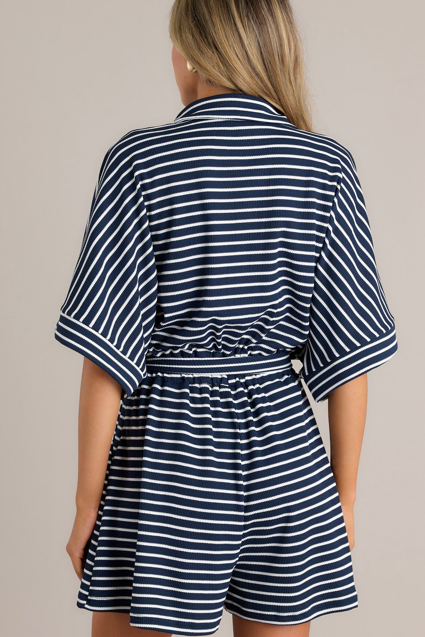 Back view of this Casual navy and white romper with short sleeves, button front, and waist tie.