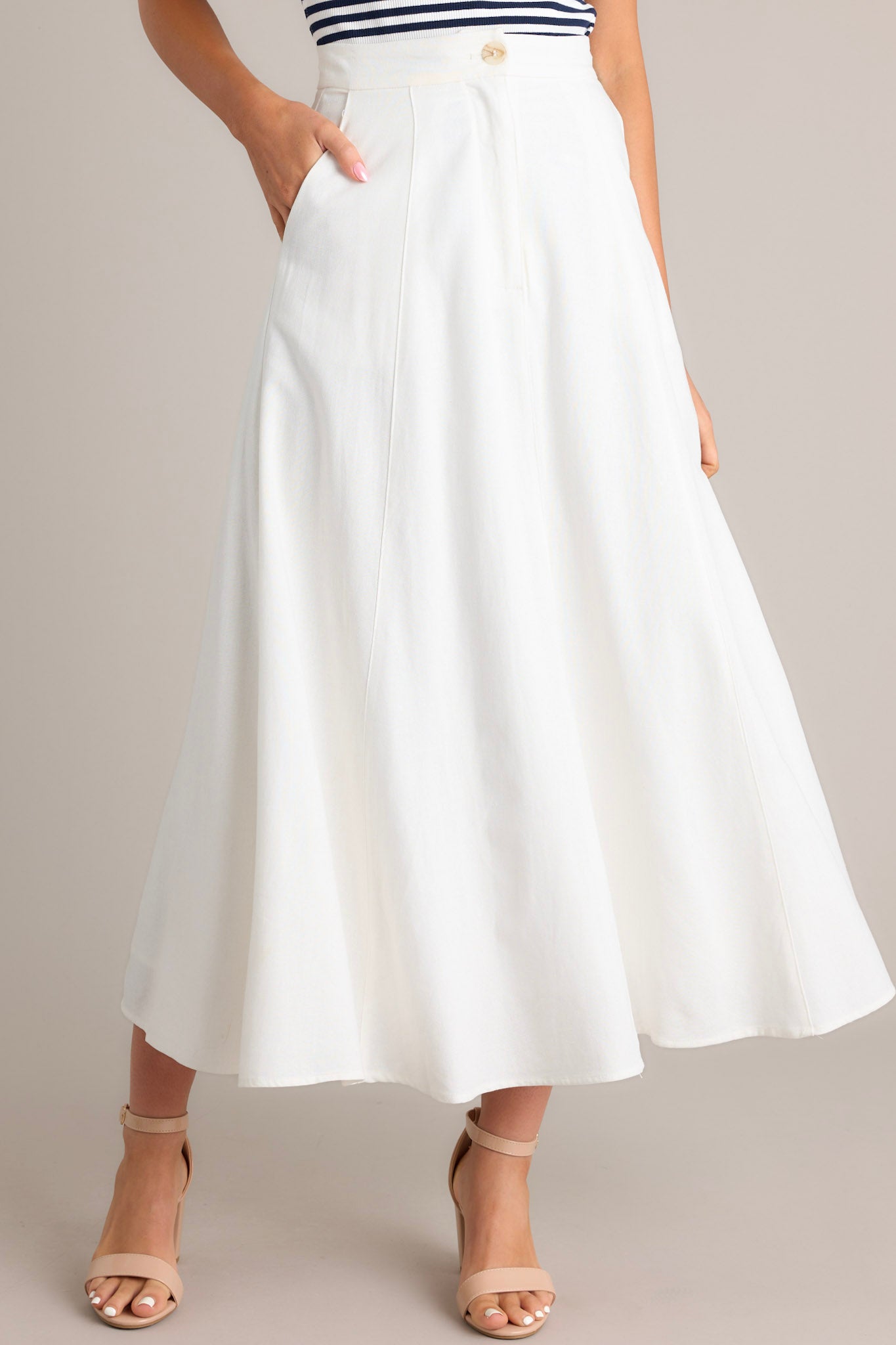 Front view of this ivory midi skirt that features a high waisted design, a button & zipper closure, functional hip pockets, visible front & back seams, and a flowing silhouette.