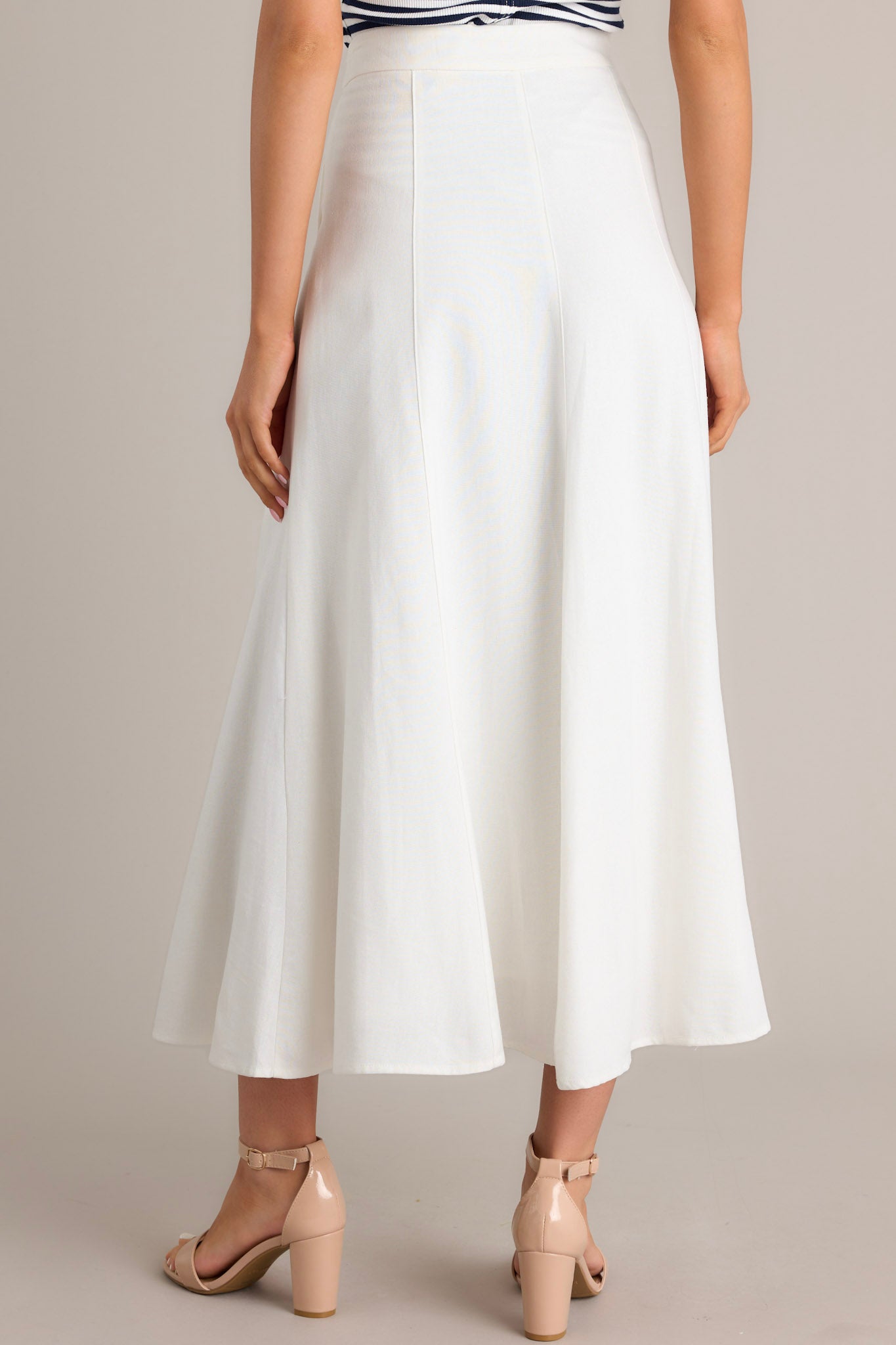 Back view of this ivory midi skirt that features a high waisted design, a button & zipper closure, functional hip pockets, visible front & back seams, and a flowing silhouette.