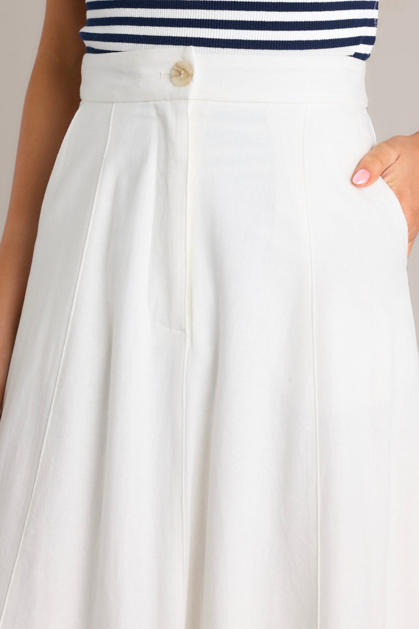 Close up view of the detailing of this ivory midi skirt that features a high waisted design, a button & zipper closure, functional hip pockets, visible front & back seams, and a flowing silhouette.