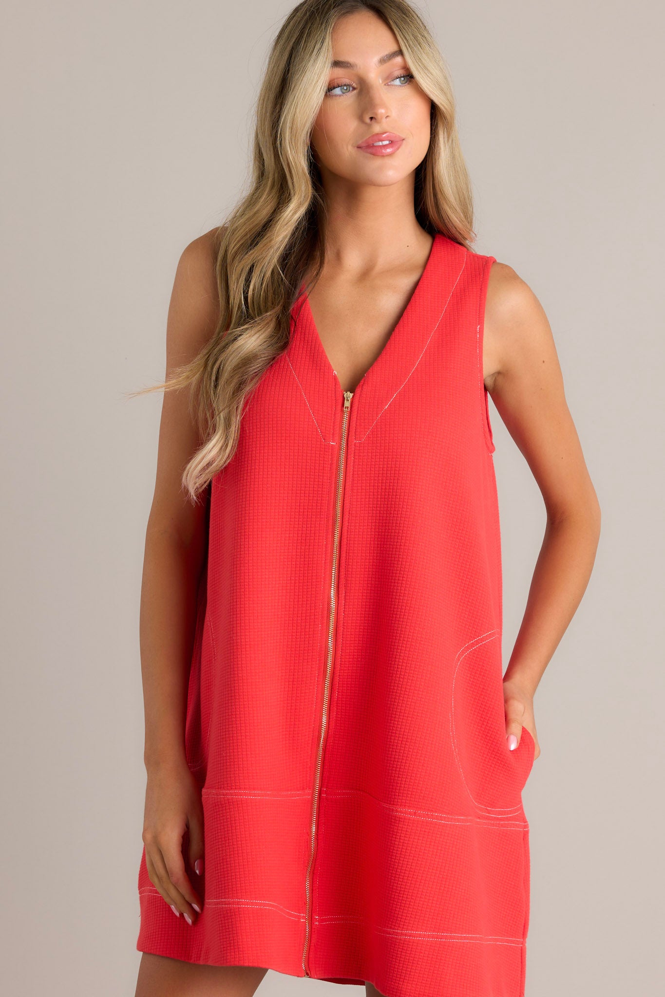 Close up view of this sleeveless, A-line coral dress with a front zipper detail and two large pockets, featuring a loose and casual fit.