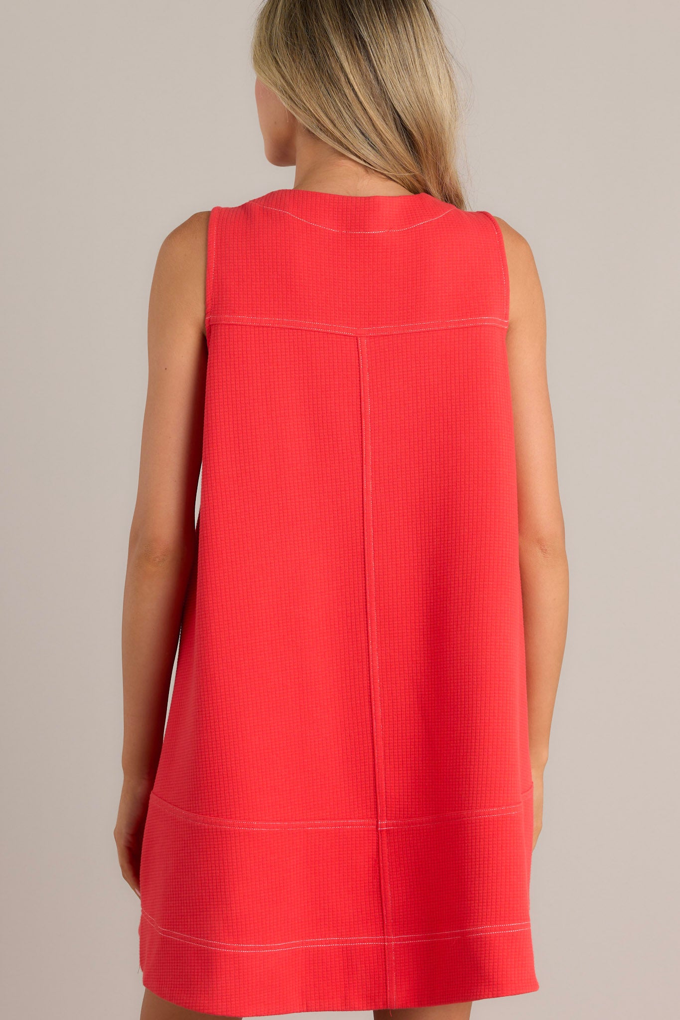 Back view of this sleeveless, A-line coral dress with a front zipper detail and two large pockets, featuring a loose and casual fit.