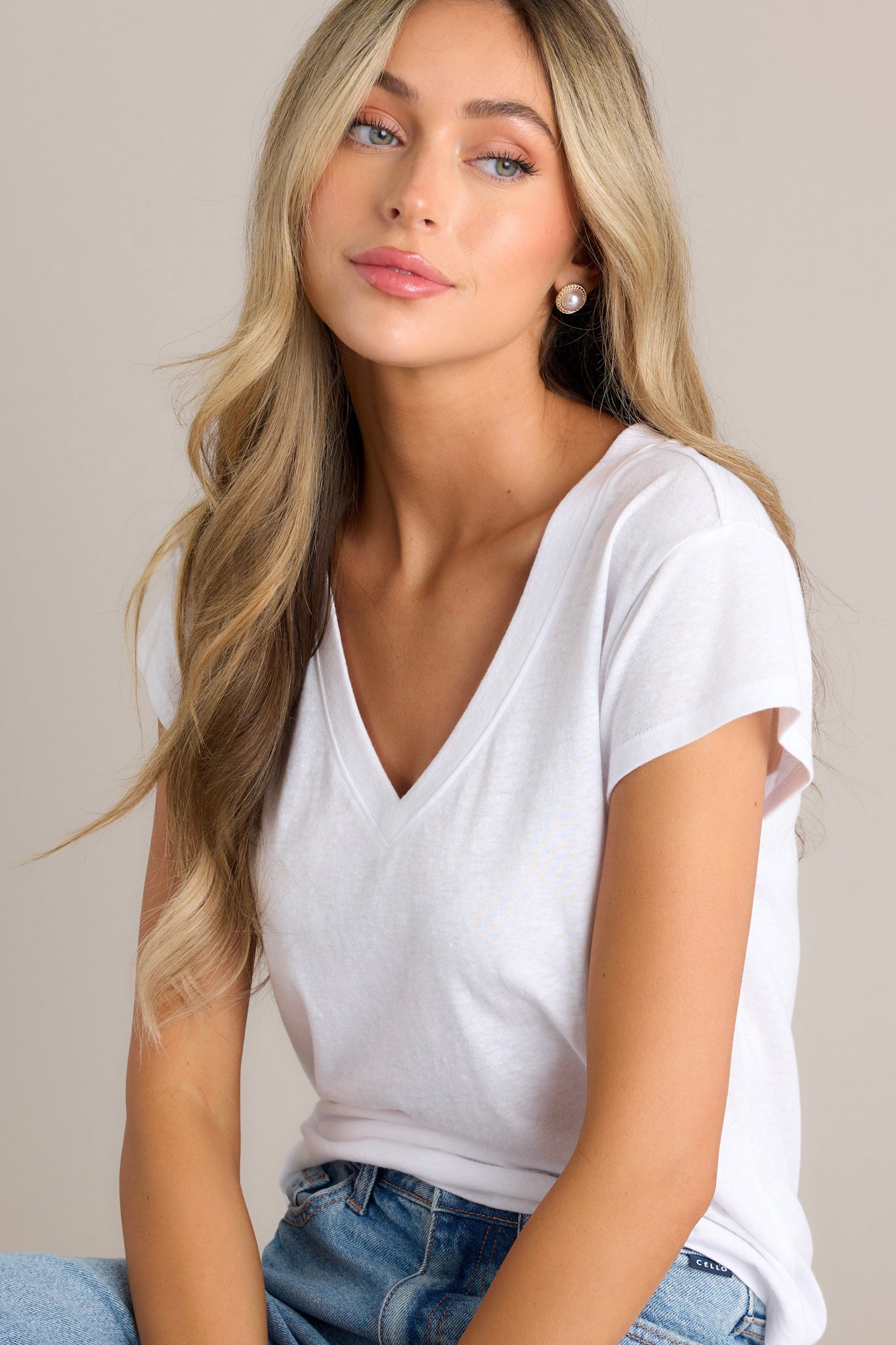 Seated front view of the neckline of this white tee that features a v-neckline, a soft & lightweight fabric, a versatile design, and loose short sleeves.