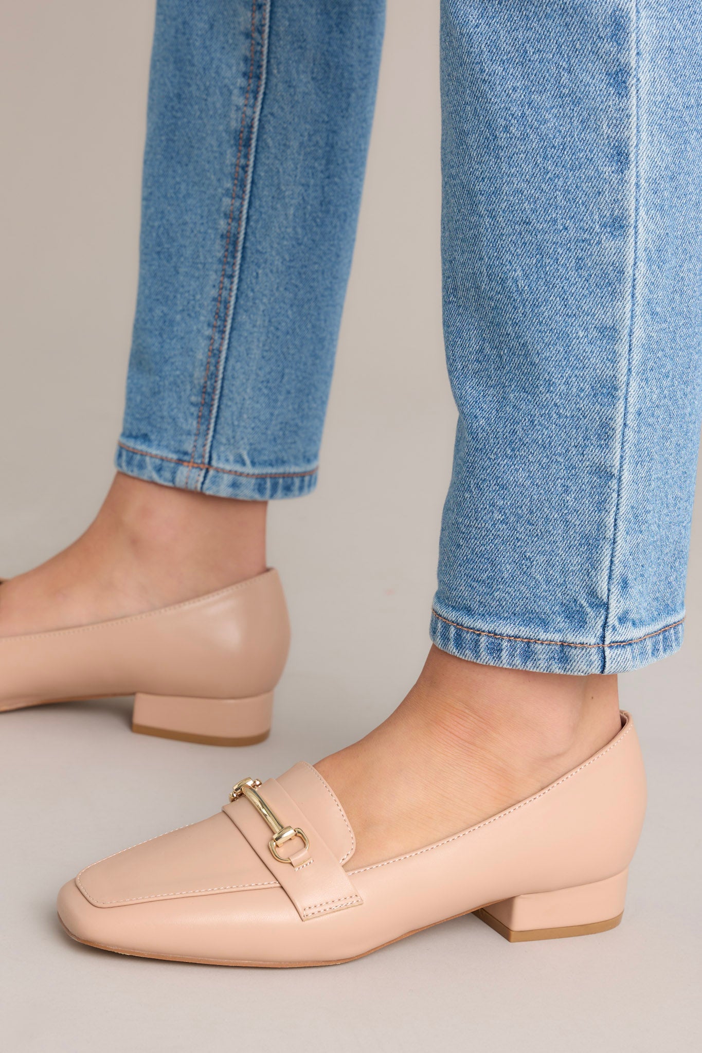 These beige loafers feature a slip on design, a small heel, a square toe, and gold hardware.
