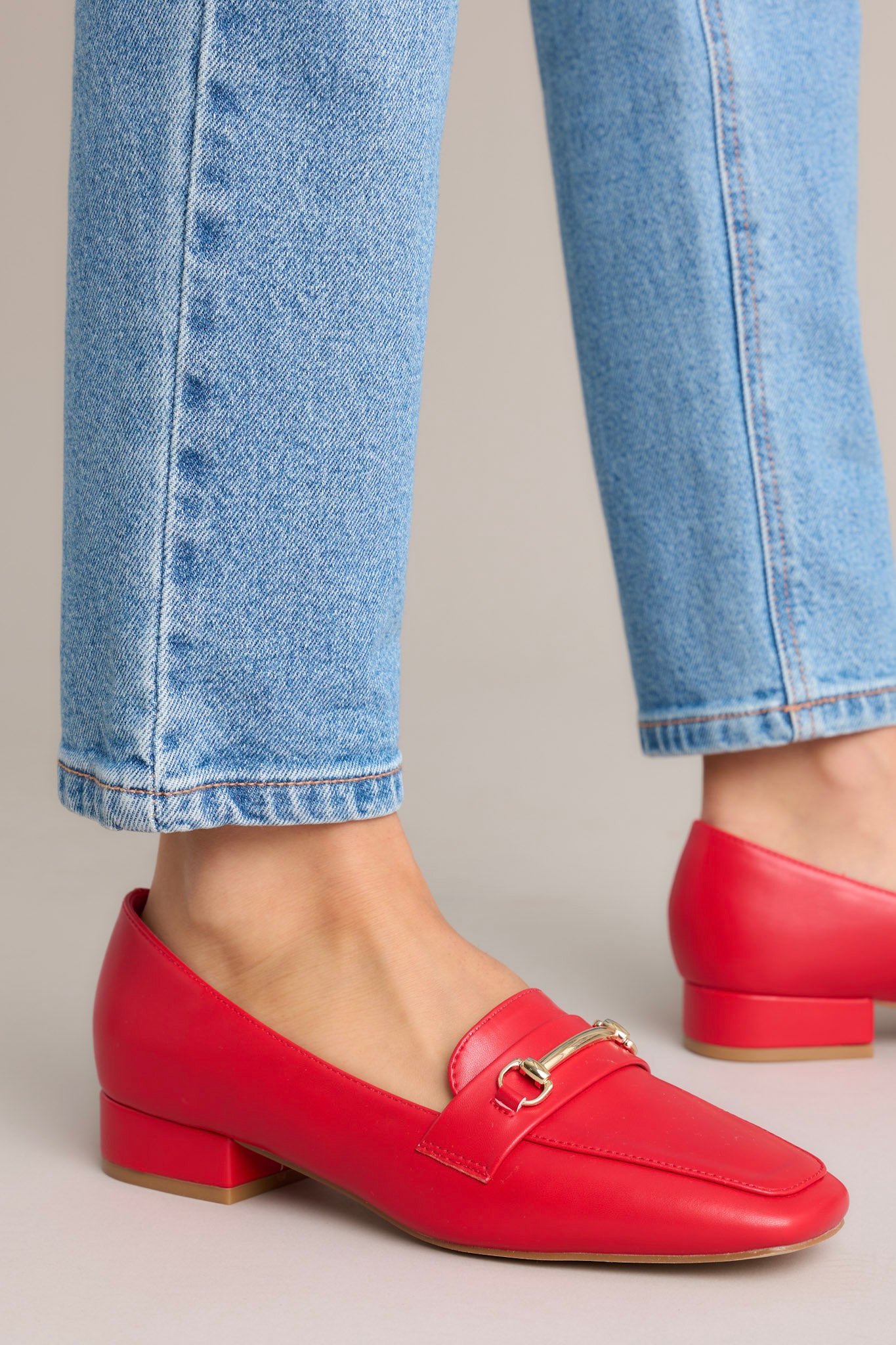 Close up view of these red loafers that feature a slip on design, a small heel, a square toe, and gold hardware.