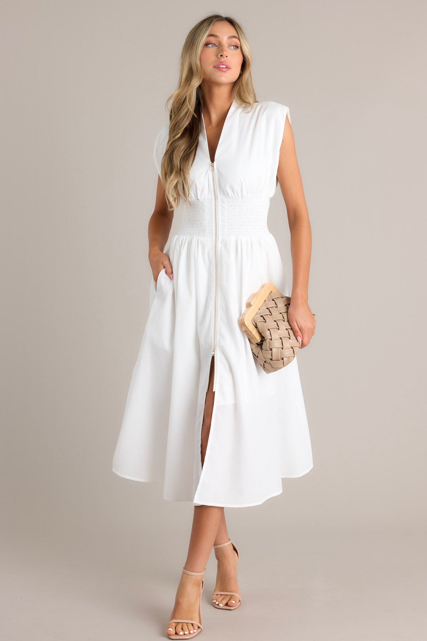 Full body view of a white dress with a V-neckline, cap sleeves, a zippered front, and a cinched waist with shirred detailing, featuring a flowing midi-length skirt with a front slit, highlighting its elegant and stylish design.